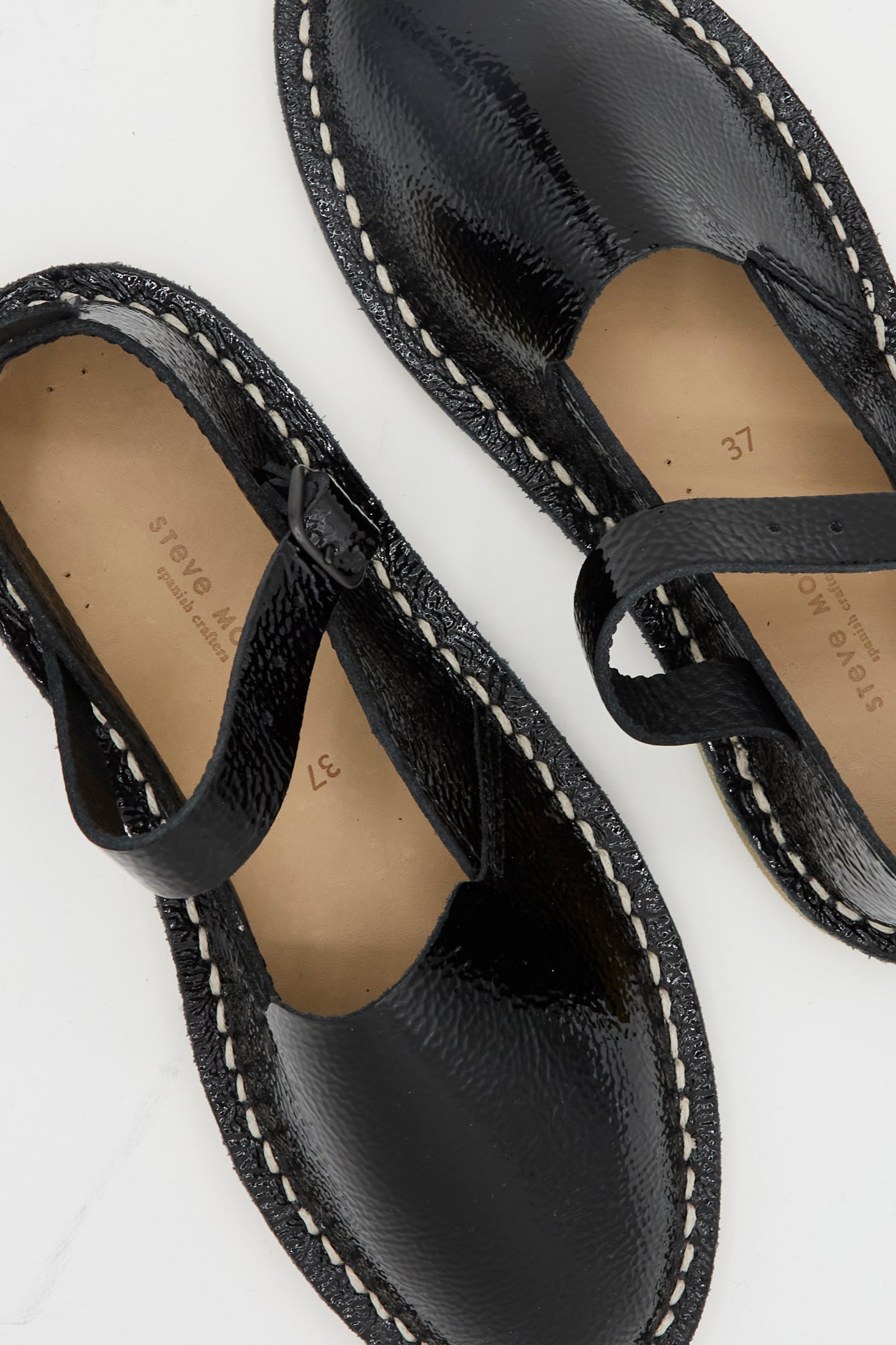 The Steve Mono Mary Jane in Glossy Black features white stitching, tan insoles, and a recycled rubber sole, shown on a white surface.