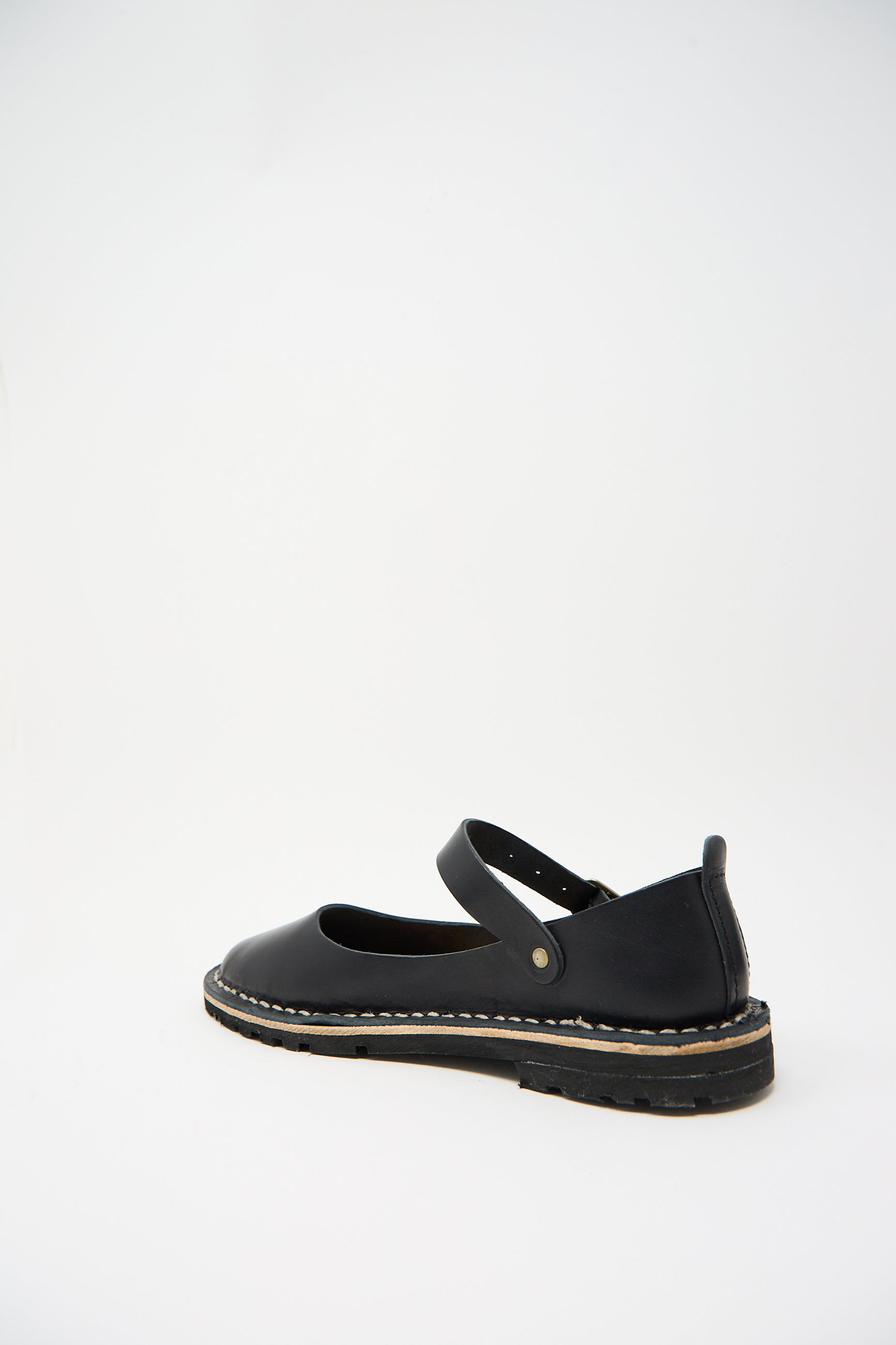 A single black leather flat shoe with a strap and stitching detail, viewed from the side against a plain white background. This Steve Mono Vegetable Tanned Calfskin Artisanal Sandal in Black is crafted from vegetable-tanned calfskin leather, showcasing both sustainability and craftsmanship.