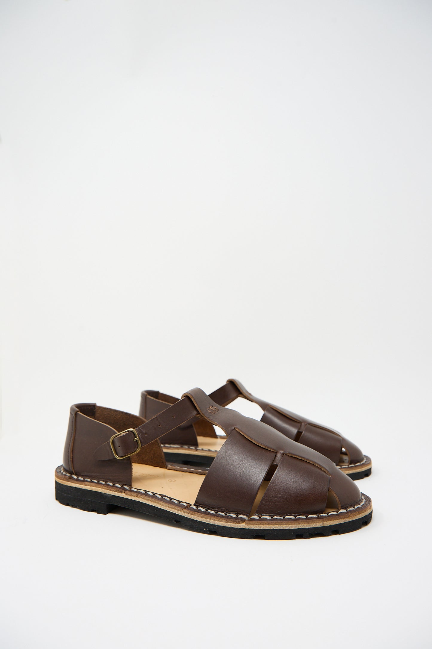 A pair of the Steve Mono Vegetable Tanned Calfskin Artisanal Sandal in Coffee with crossed straps and buckle closures, placed against a plain white background.