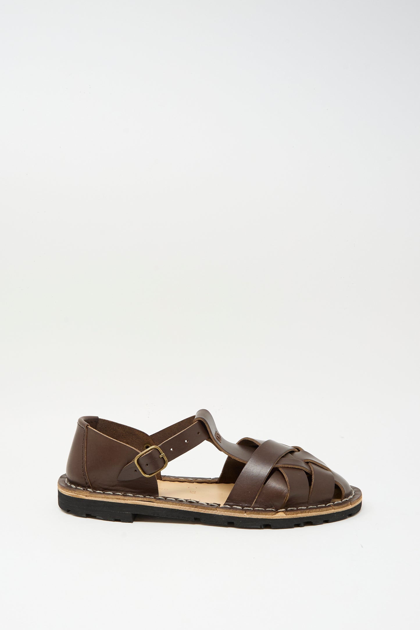 The Steve Mono Woven Leather Sandals in Dark Coffee feature a buckle strap and closed toe design, crafted from vegetable tanned leather in Spain. Shown against a plain white background.