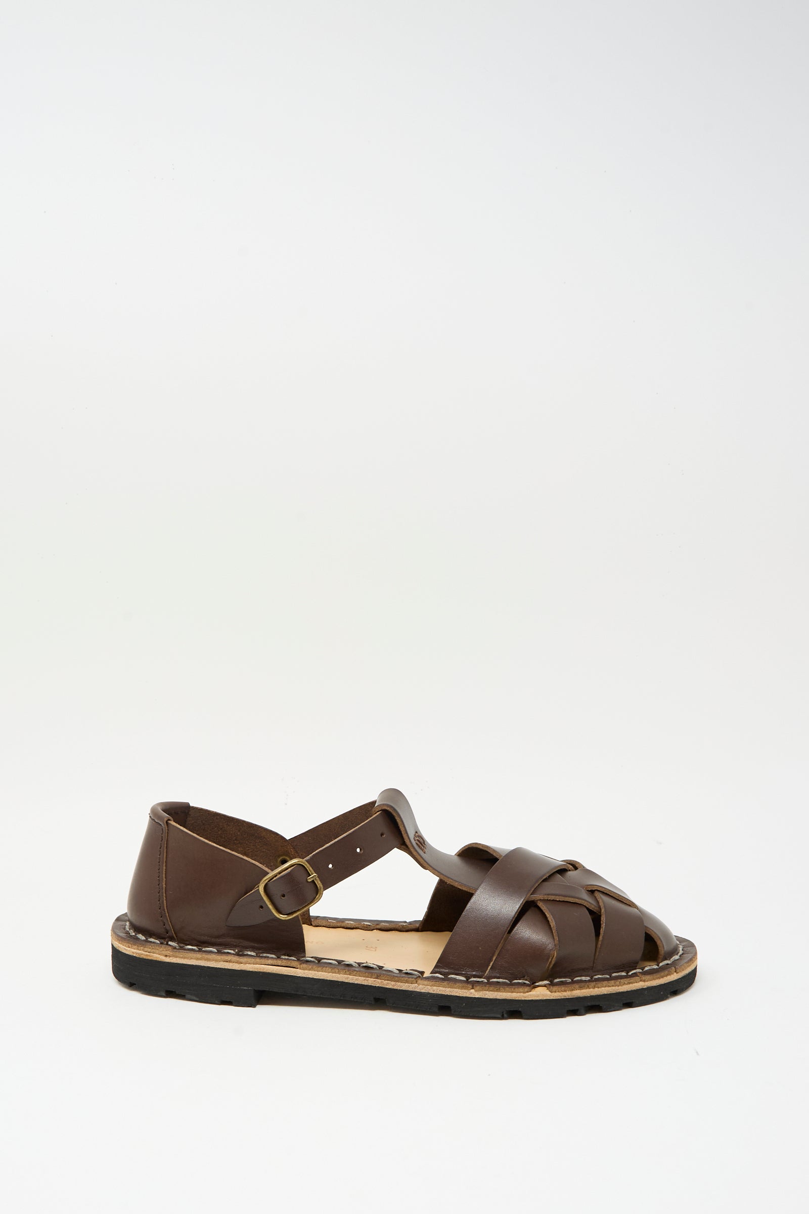 The Steve Mono Woven Leather Sandals in Dark Coffee feature a buckle strap and closed toe design, crafted from vegetable tanned leather in Spain. Shown against a plain white background.