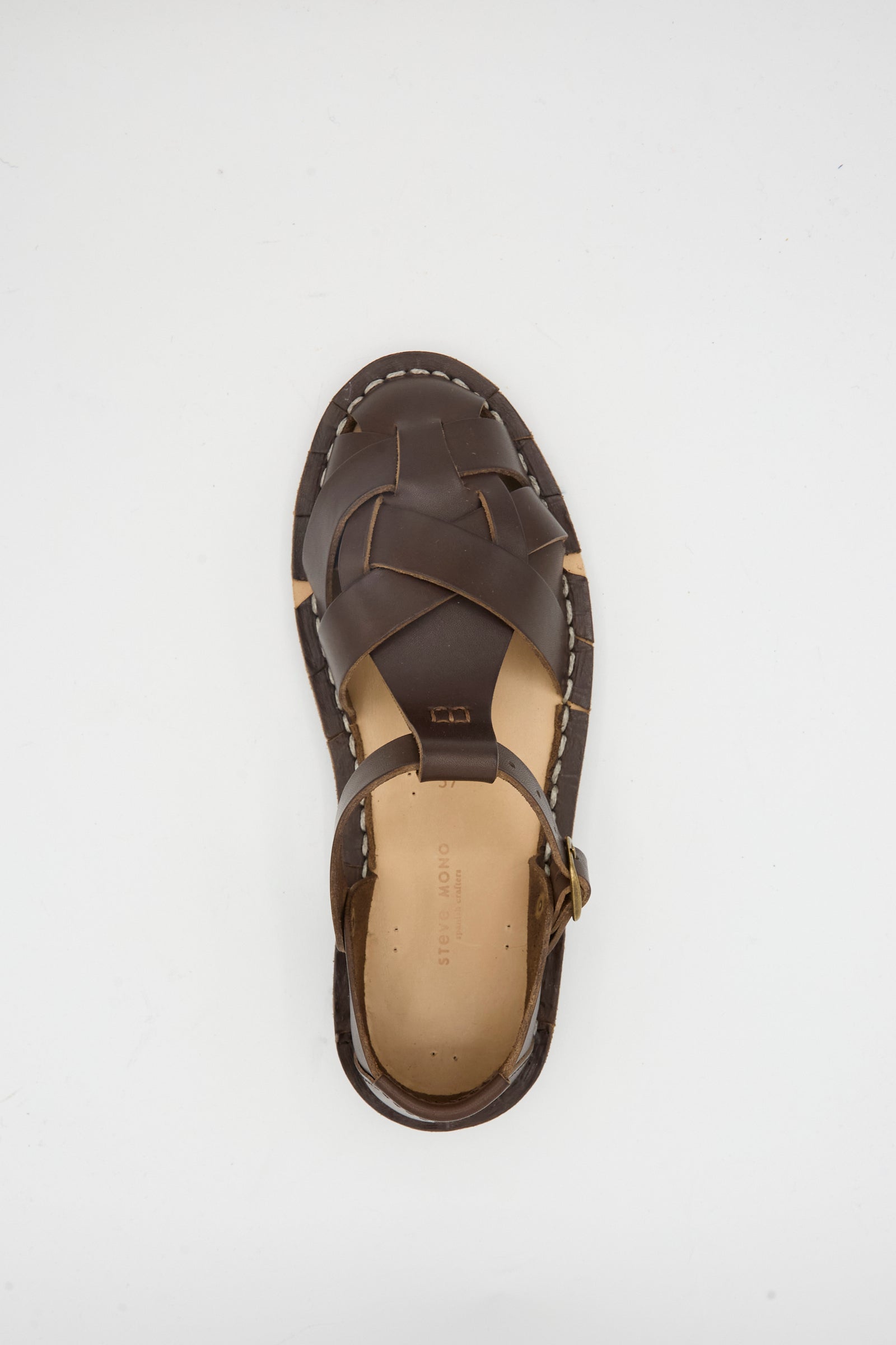 The Steve Mono Woven Leather Sandals in Dark Coffee feature a woven design and ankle strap, crafted from vegetable tanned leather. Shown is a single sandal photographed from above on a white background.