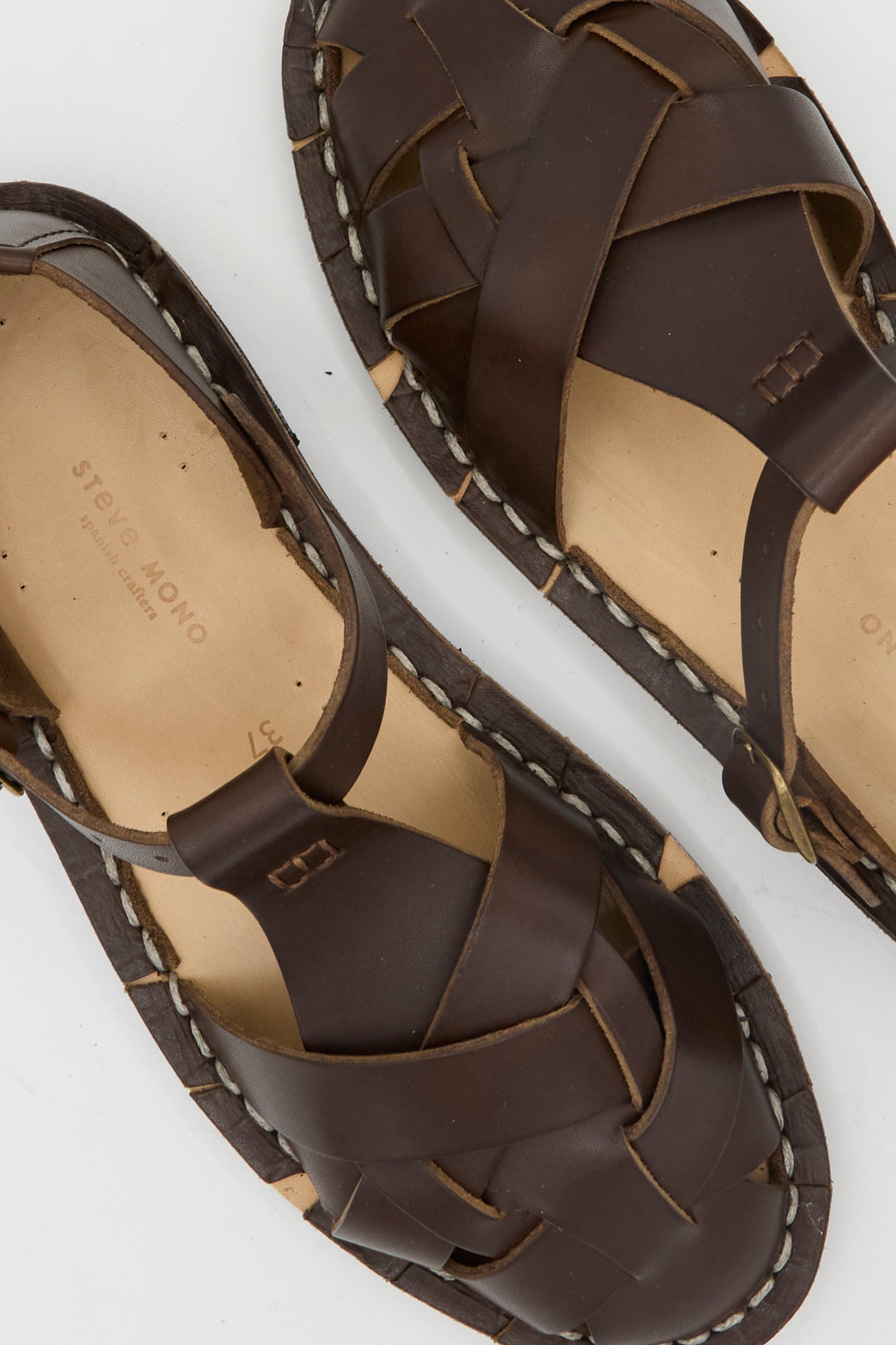 The Steve Mono Woven Leather Sandals in Dark Coffee are artisanal Spanish sandals with a woven design and cream stitching on the soles, crafted from vegetable-tanned leather and shown in a top-down view.