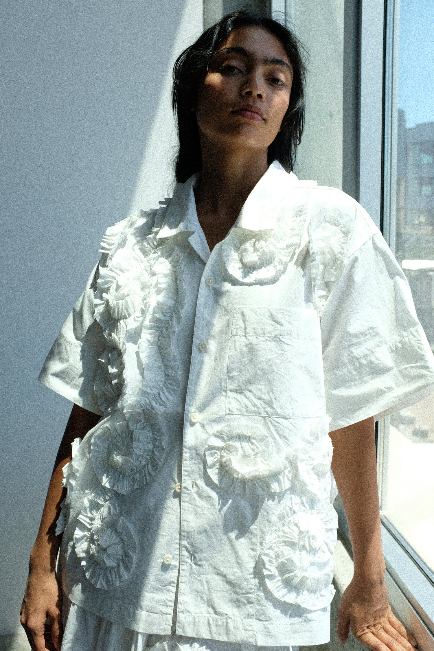 Person wearing a Story mfg. Hand Applique Greetings Shirt in Ecru Fossil standing by a window.