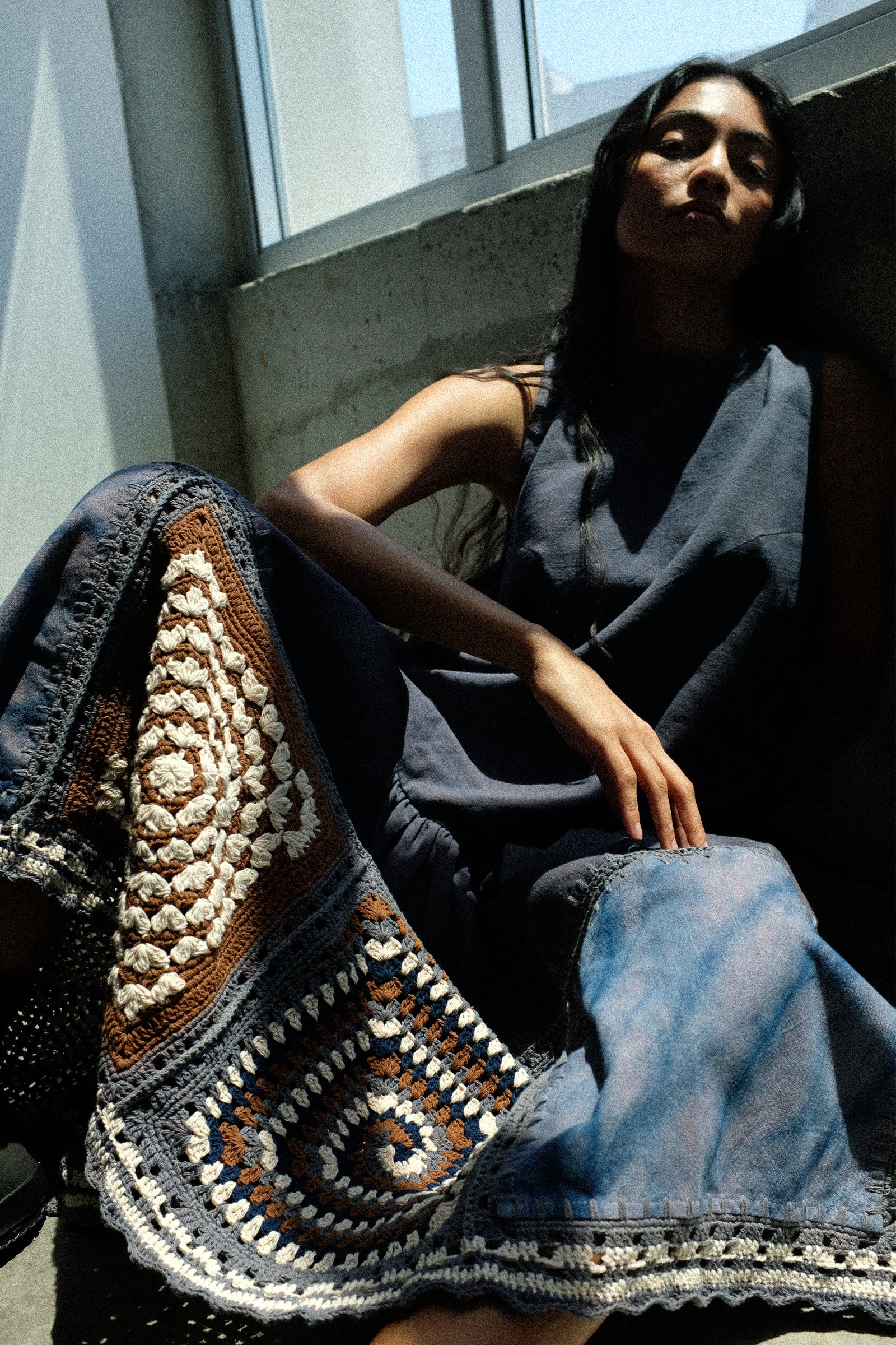 A woman sitting on the floor next to a window wearing Story mfg. Snowdrop Dress in Cosmic Crochet.