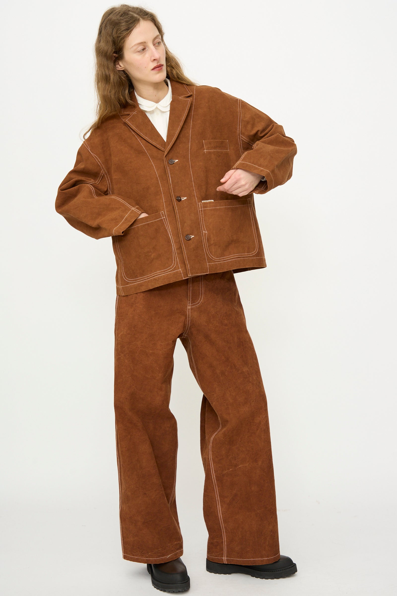 Wearing the Story mfg. Canvas Cove Jacket in Brown Wonky-Wear, matching wide-leg pants with white stitching, a white shirt, and black shoes, this person stands against a plain white background.