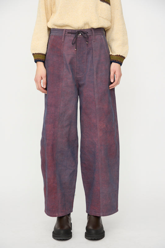 A person stands against a plain background wearing a beige sweater, black boots, and Story mfg.’s Canvas Document Pant in Ancient Purple.