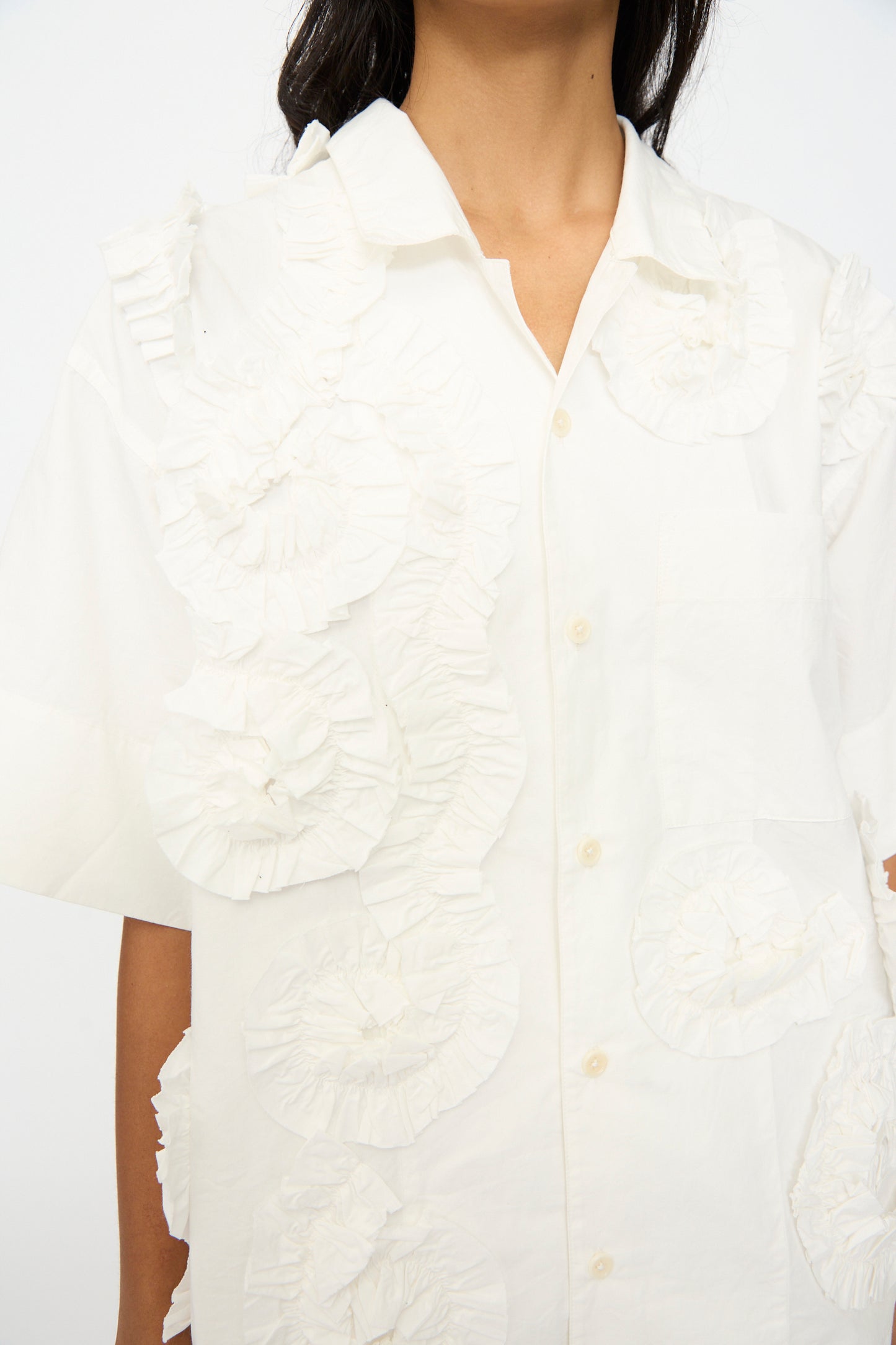 A person wearing the Story mfg. Hand Applique Greetings Shirt in Ecru Fossil, an oversized shirt with large, textured front ruffles.