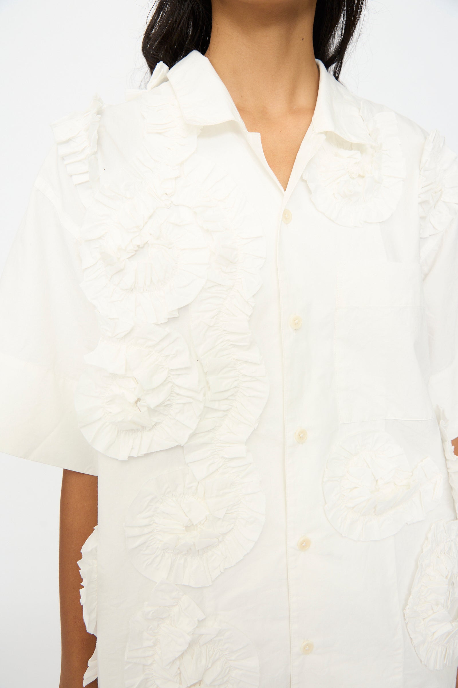 A person wearing the Story mfg. Hand Applique Greetings Shirt in Ecru Fossil, an oversized shirt with large, textured front ruffles.