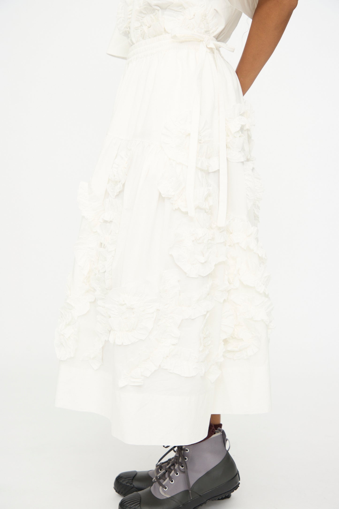 Model wears the Story mfg. Hand Applique Orbit Skirt in Ecru Fossil with gray lace-up boots, standing against a plain white background.