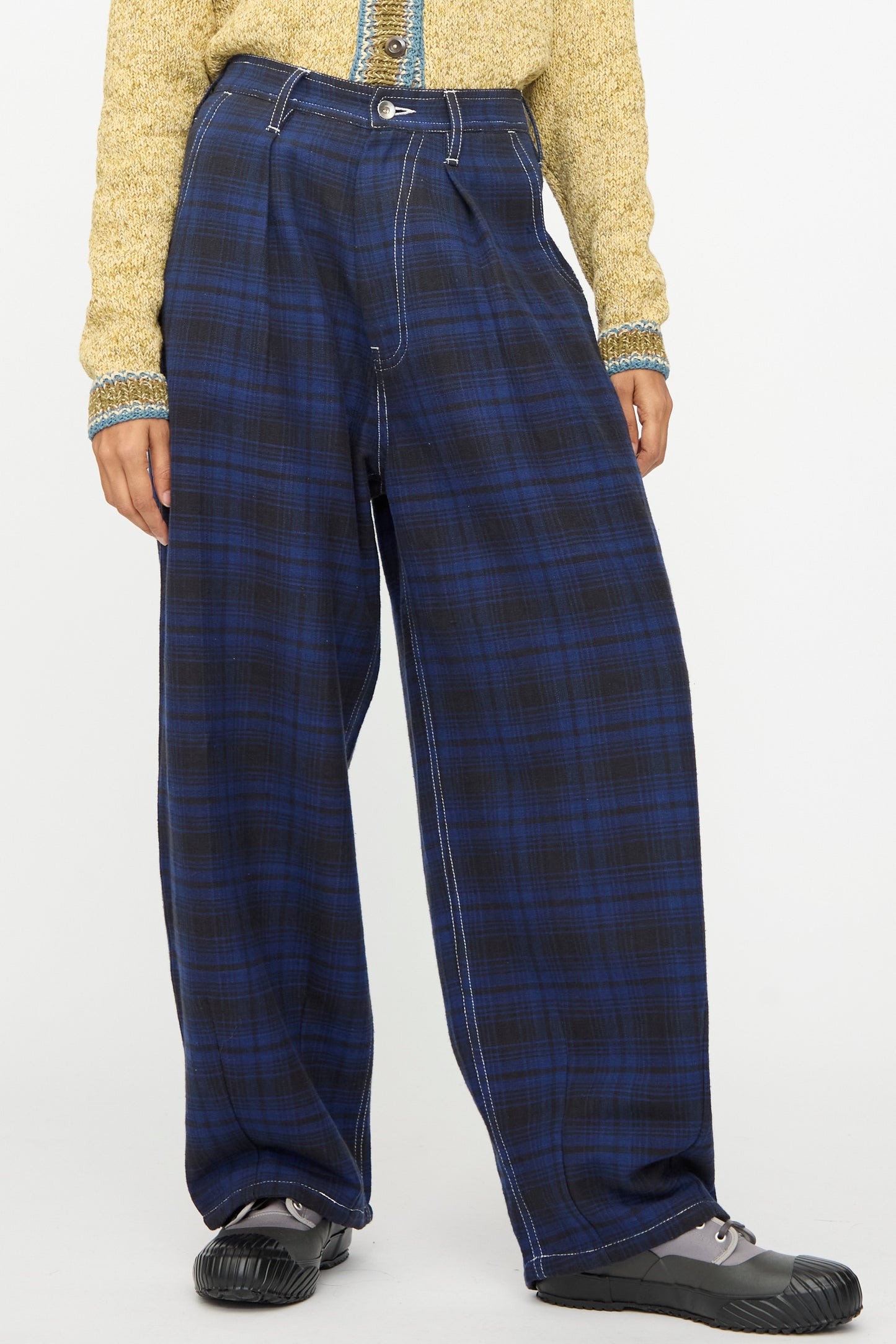 A person wearing Story mfg.'s Hand Woven Lush Pants in Solar Check with a yellow textured long-sleeve top and black shoes, standing against a plain background.