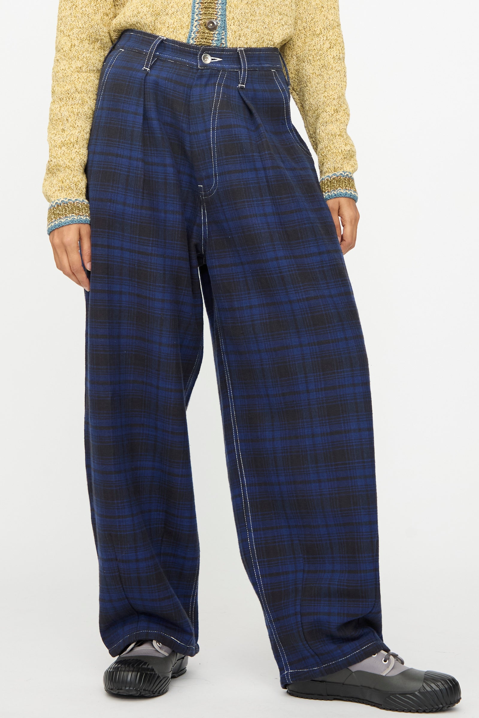 A person wearing Story mfg.'s Hand Woven Lush Pants in Solar Check with a yellow textured long-sleeve top and black shoes, standing against a plain background.