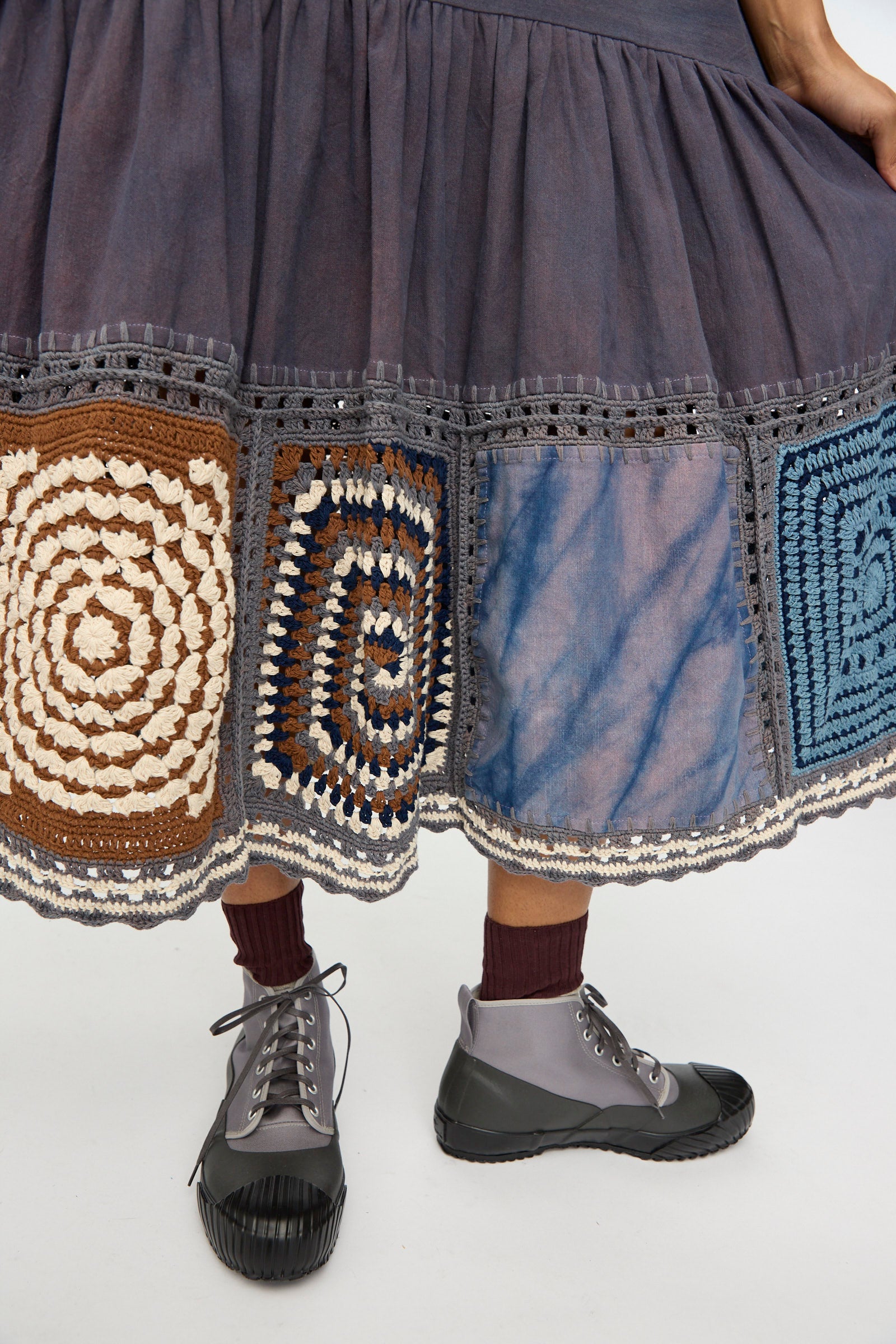 Person wearing the Story mfg. Snowdrop Dress in Cosmic Crochet and gray lace-up boots with burgundy socks, standing on a light background.