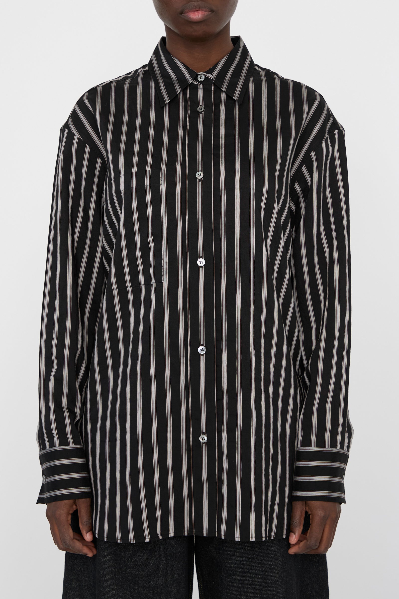 A person is seen wearing the Archive Modal Stripe Leto Shirt in Darkest Navy, an oversized piece from Studio Nicholson with long sleeves and black and white vertical pinstripes.