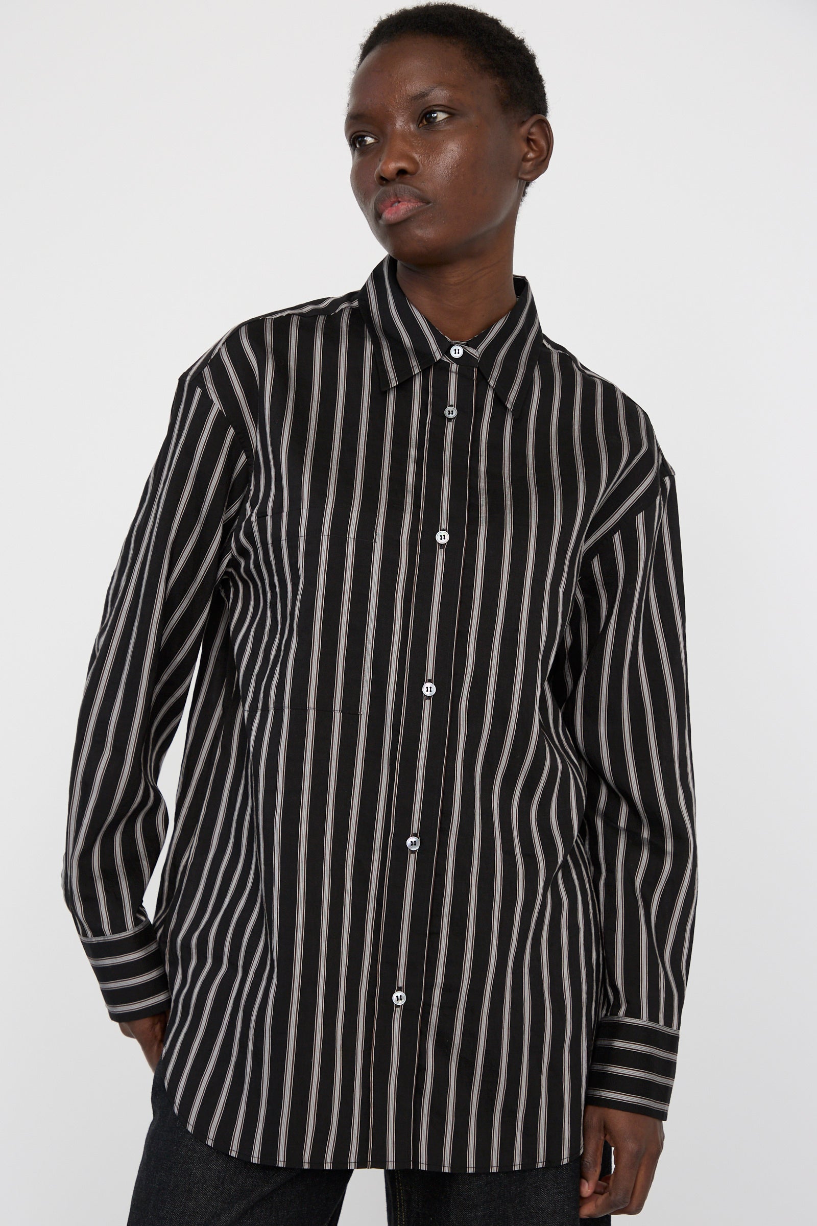 A person wearing Studio Nicholson's Archive Modal Stripe Leto Shirt in Darkest Navy stands against a plain background, seen from the hips up.  