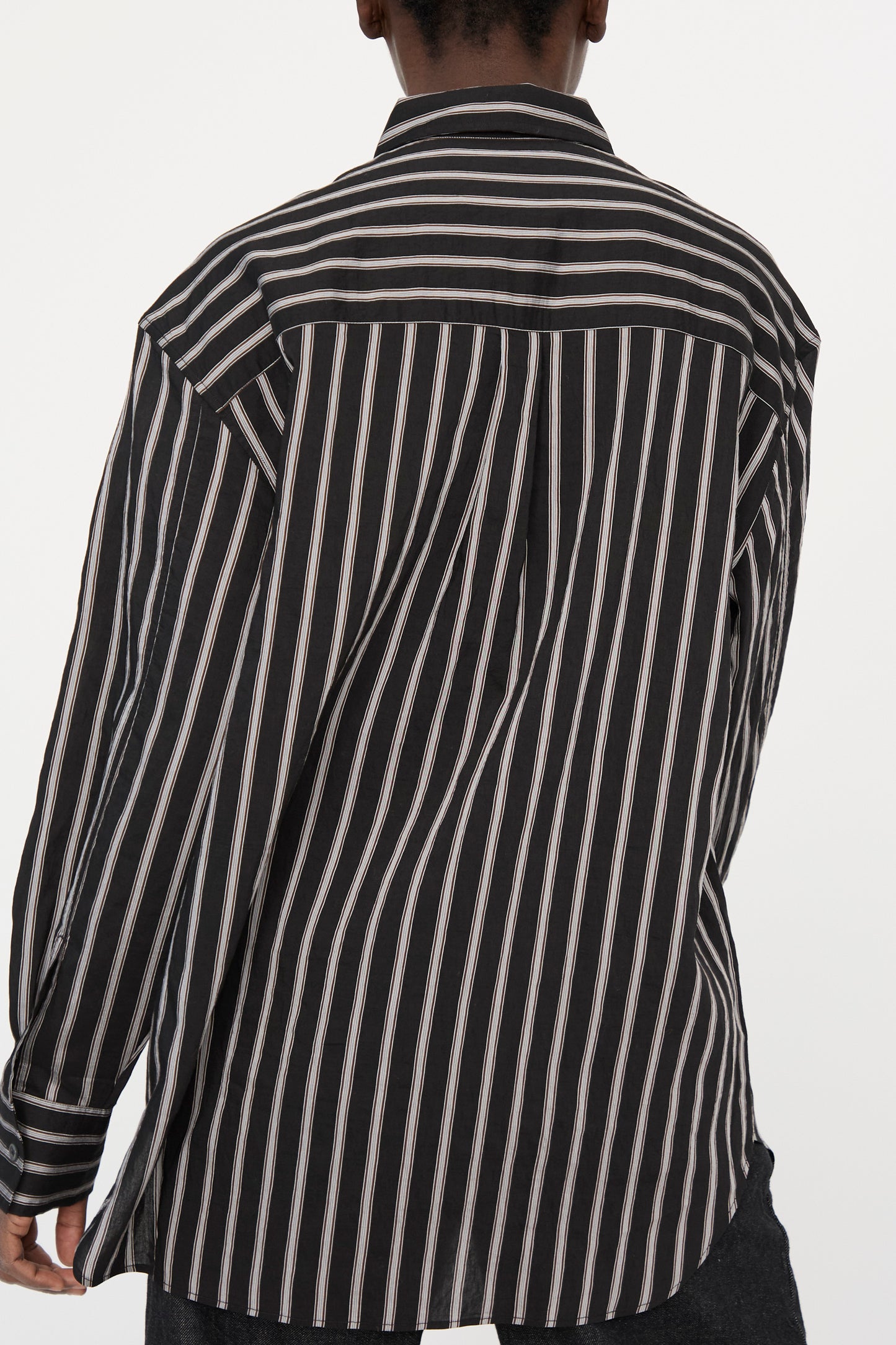 A person is seen from the back wearing the Studio Nicholson Archive Modal Stripe Leto Shirt in Darkest Navy, featuring an oversized fit and adorned with vertical pin stripes.