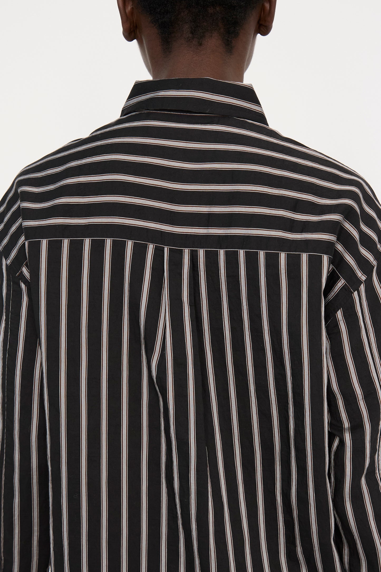 Back view of a person wearing the Archive Modal Stripe Leto Shirt in Darkest Navy from Studio Nicholson, featuring an oversized design with black and white stripes.