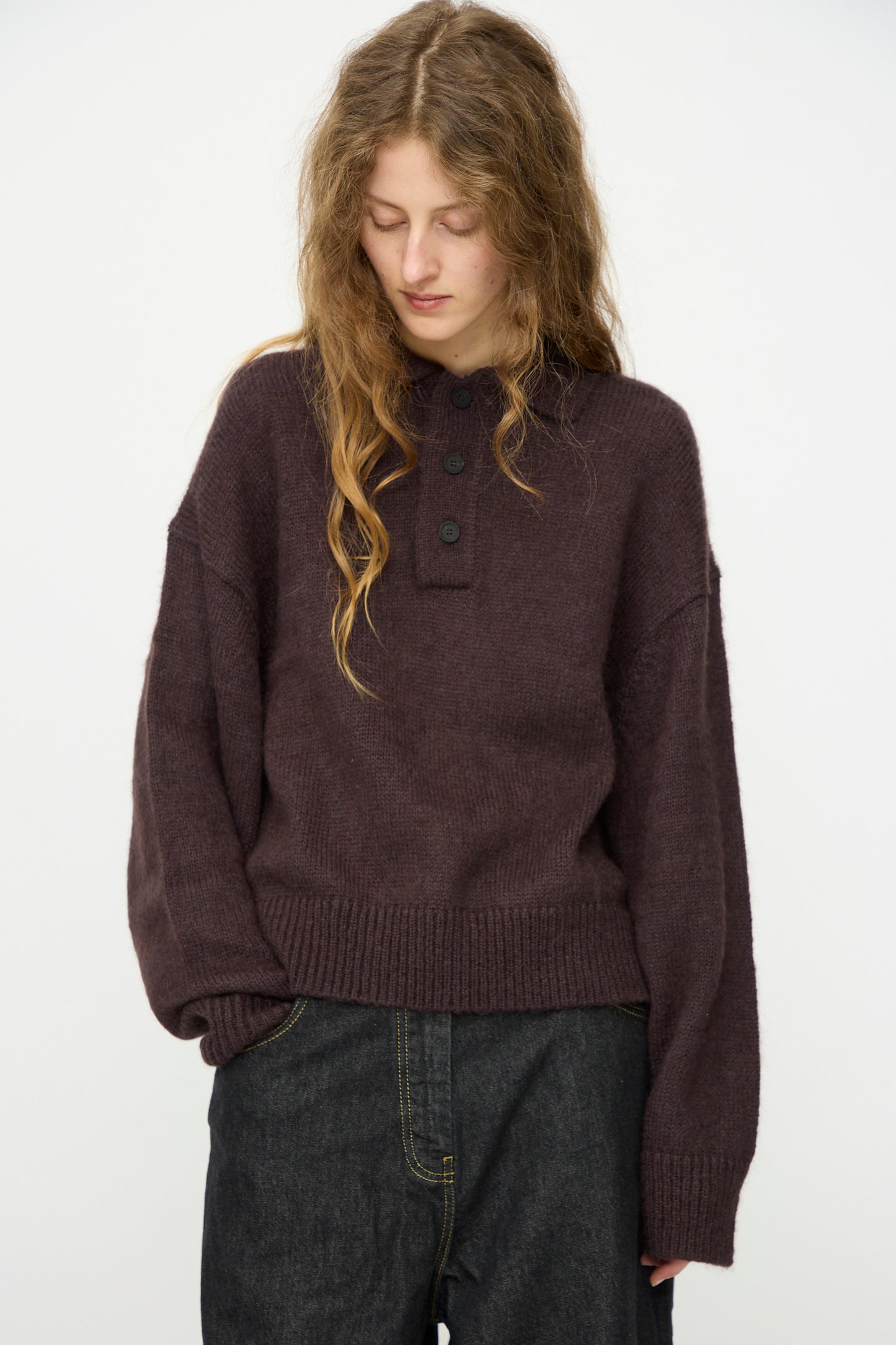 A person wearing the Studio Nicholson Brushed Mohair Dune Knit Shirt in Espresso with dark jeans stands against a plain white background, looking down.
