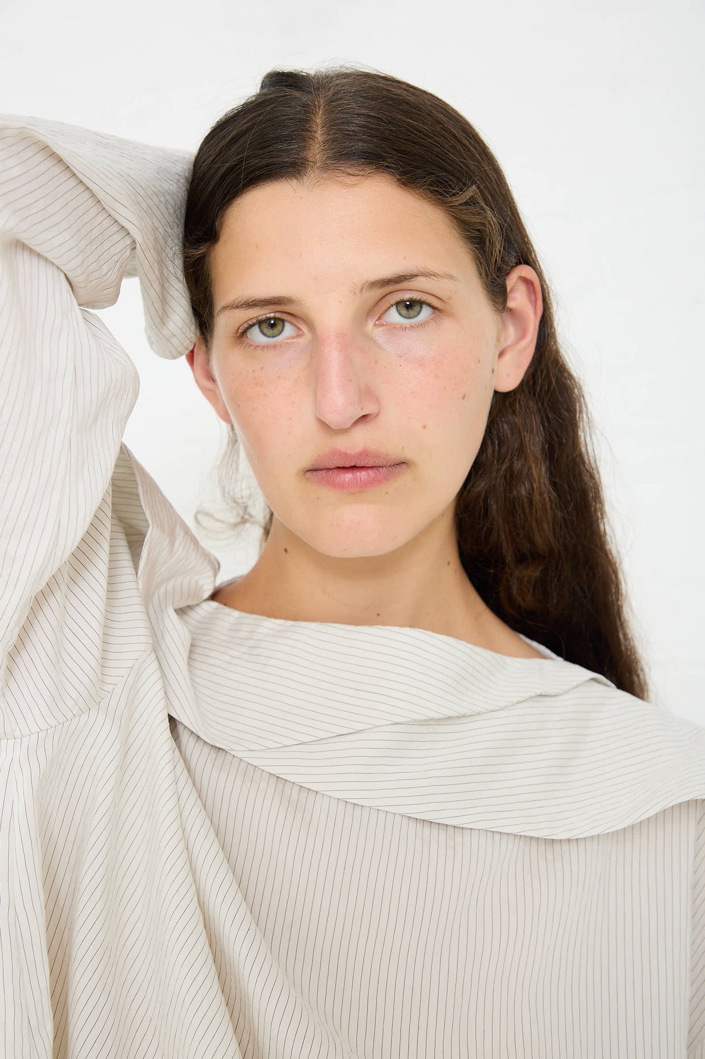 Person with long dark hair and light complexion slightly tilting their head, wearing an Emmet Drape Sleeve Top in Black and White Stripe by Studio Nicholson. Background is plain and white.