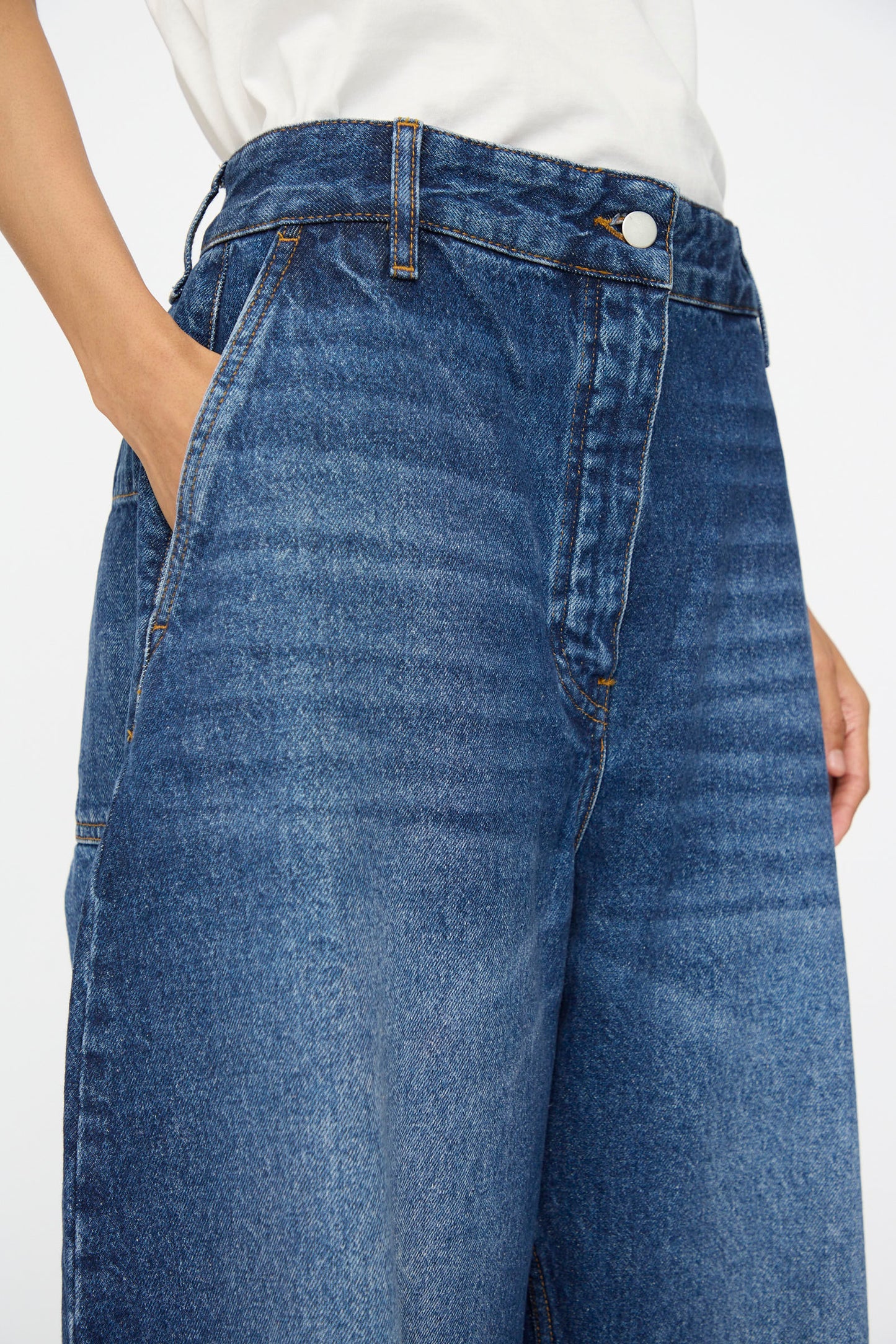 Model wears the Studio Nicholson Denim Chalco Jean in Worn Wash Indigo with a white shirt; the photo highlights the high waist and wide leg silhouette, focusing on the waist and upper thigh area.