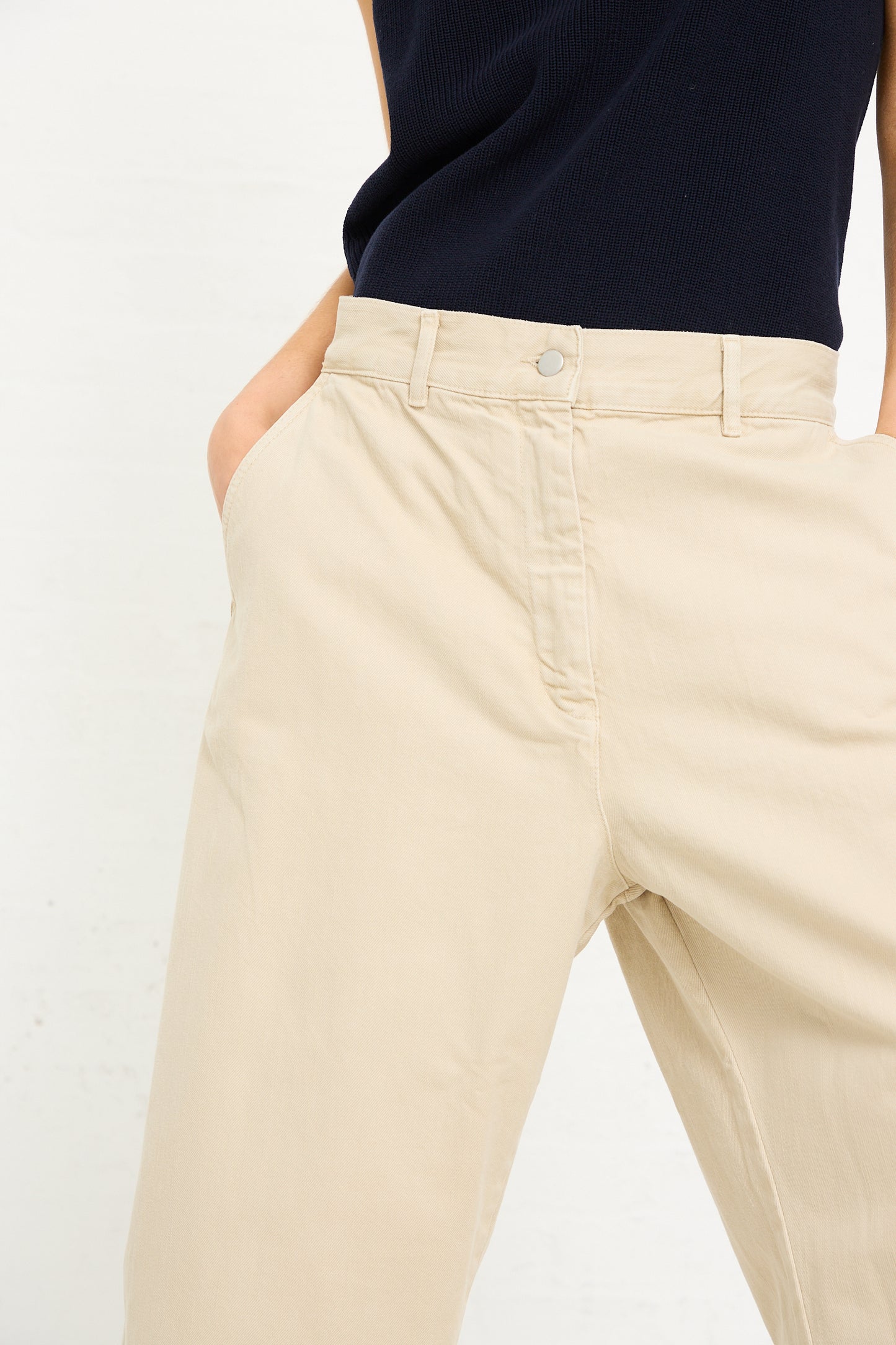 Close-up of a person wearing Studio Nicholson Denim Chalco Wide Crop Pant in Dove and a dark navy top, focusing on the button and pocket detail.