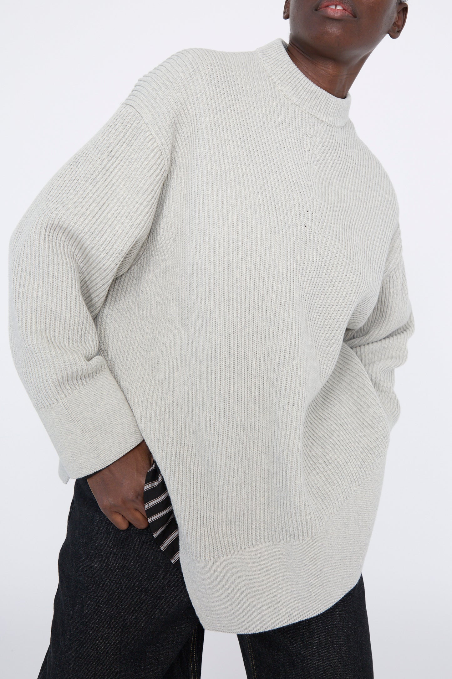 A person wearing the Studio Nicholson Dry Cotton Rib Verda Asymmetric Knit in Grey Marl and dark pants against a plain background.