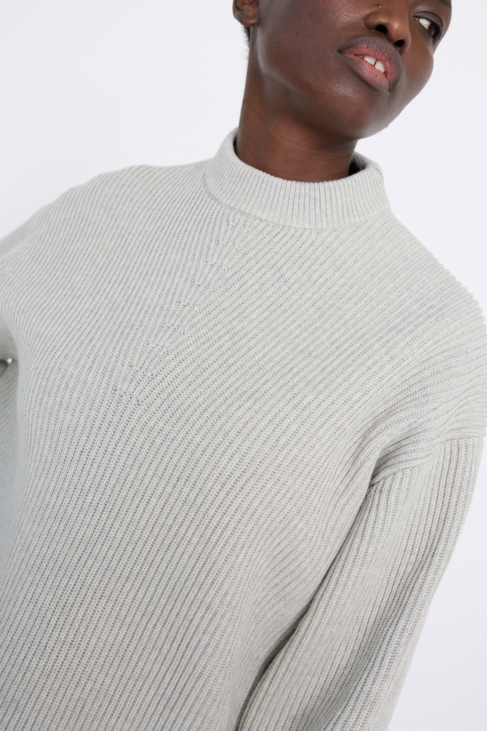 A person is wearing the Studio Nicholson Dry Cotton Rib Verda Asymmetric Knit in Grey Marl against a plain background.