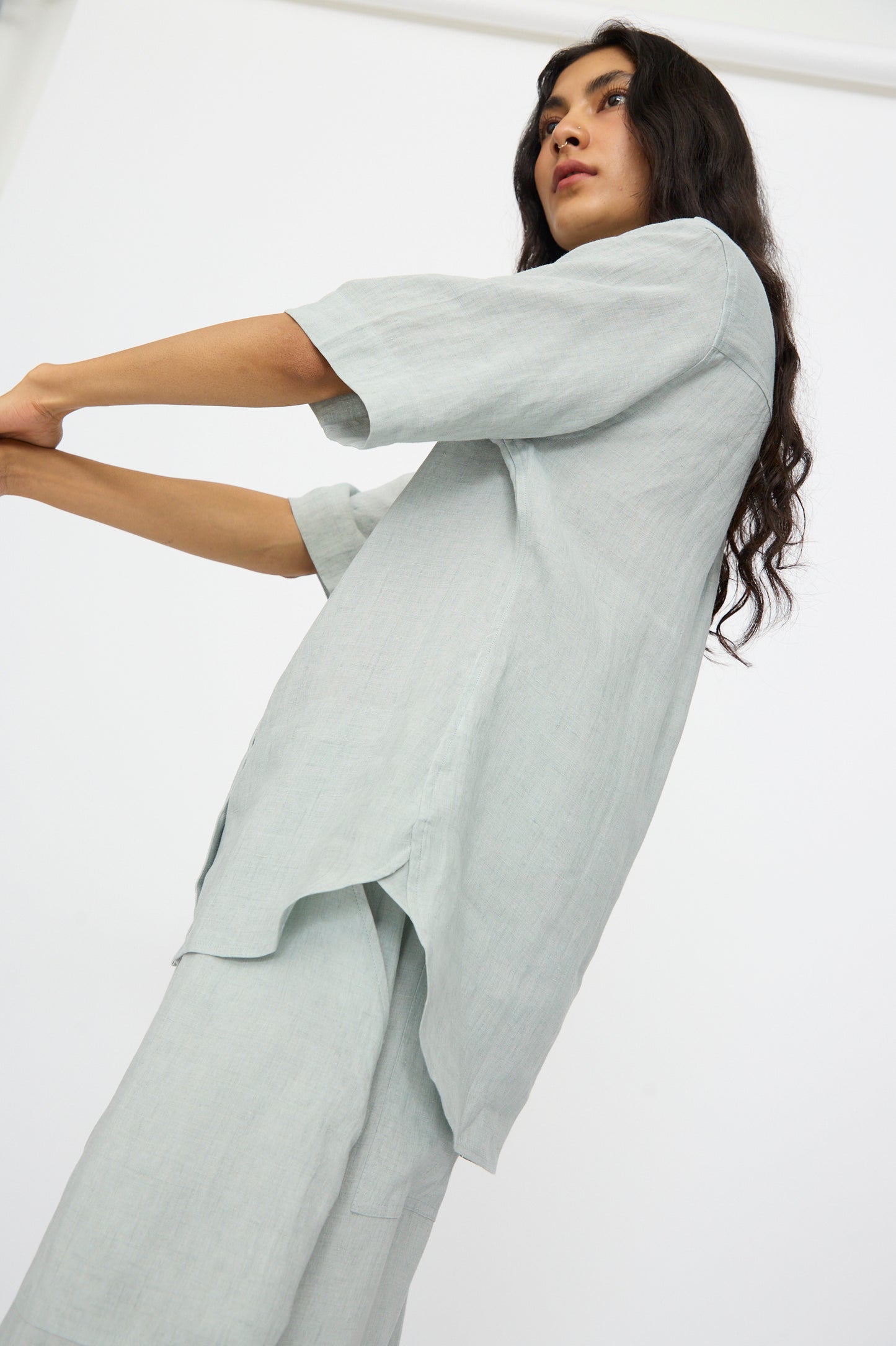 A person wears the Studio Nicholson Estes Shirt in Spearmint, a relaxed-fit, short-sleeve style, standing against a plain white background with arms extended forward and head slightly turned.
