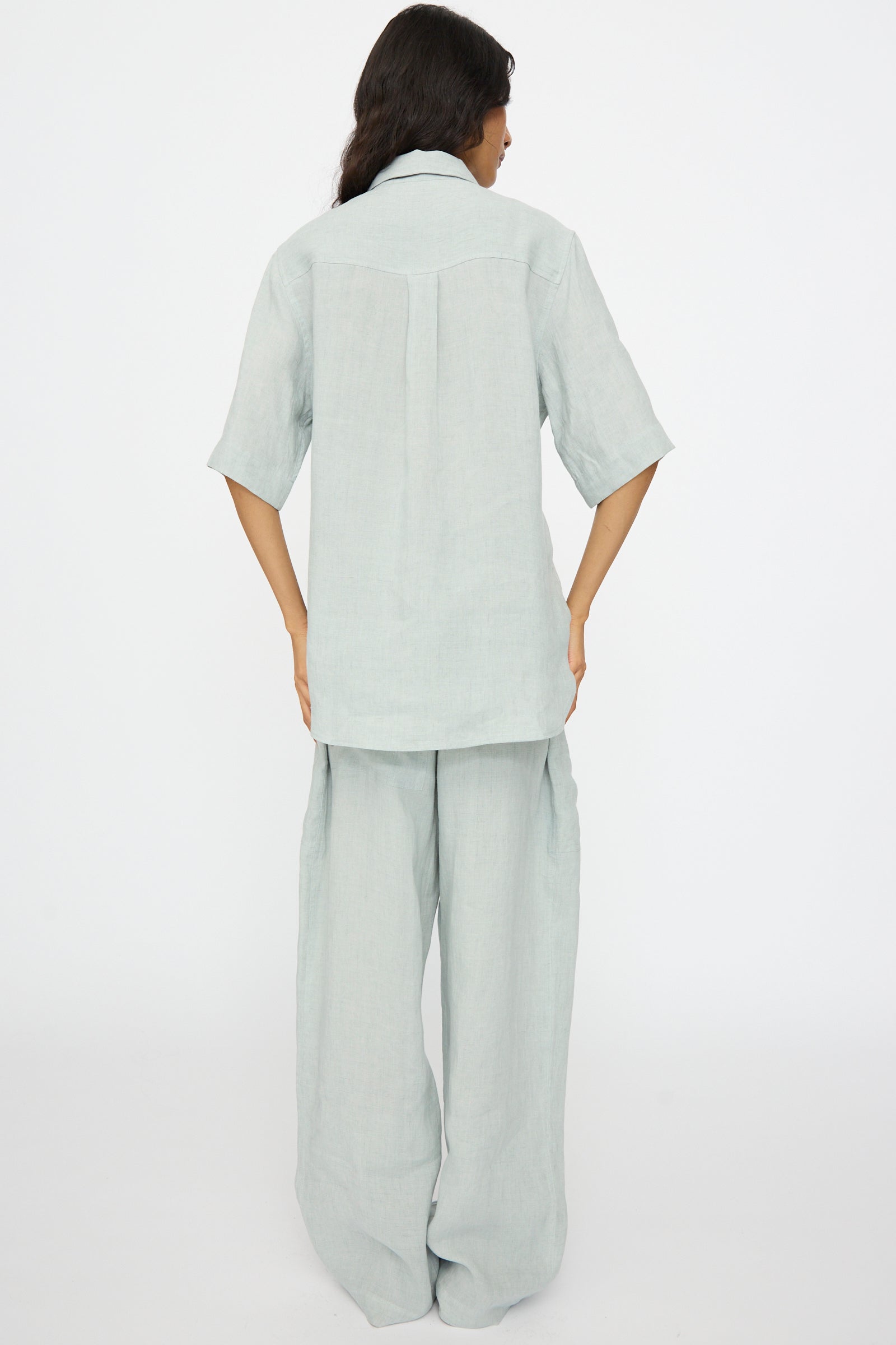 A person stands with their back to the camera, wearing the Studio Nicholson Estes Shirt in Spearmint, styled in a relaxed fit, against a plain white background.