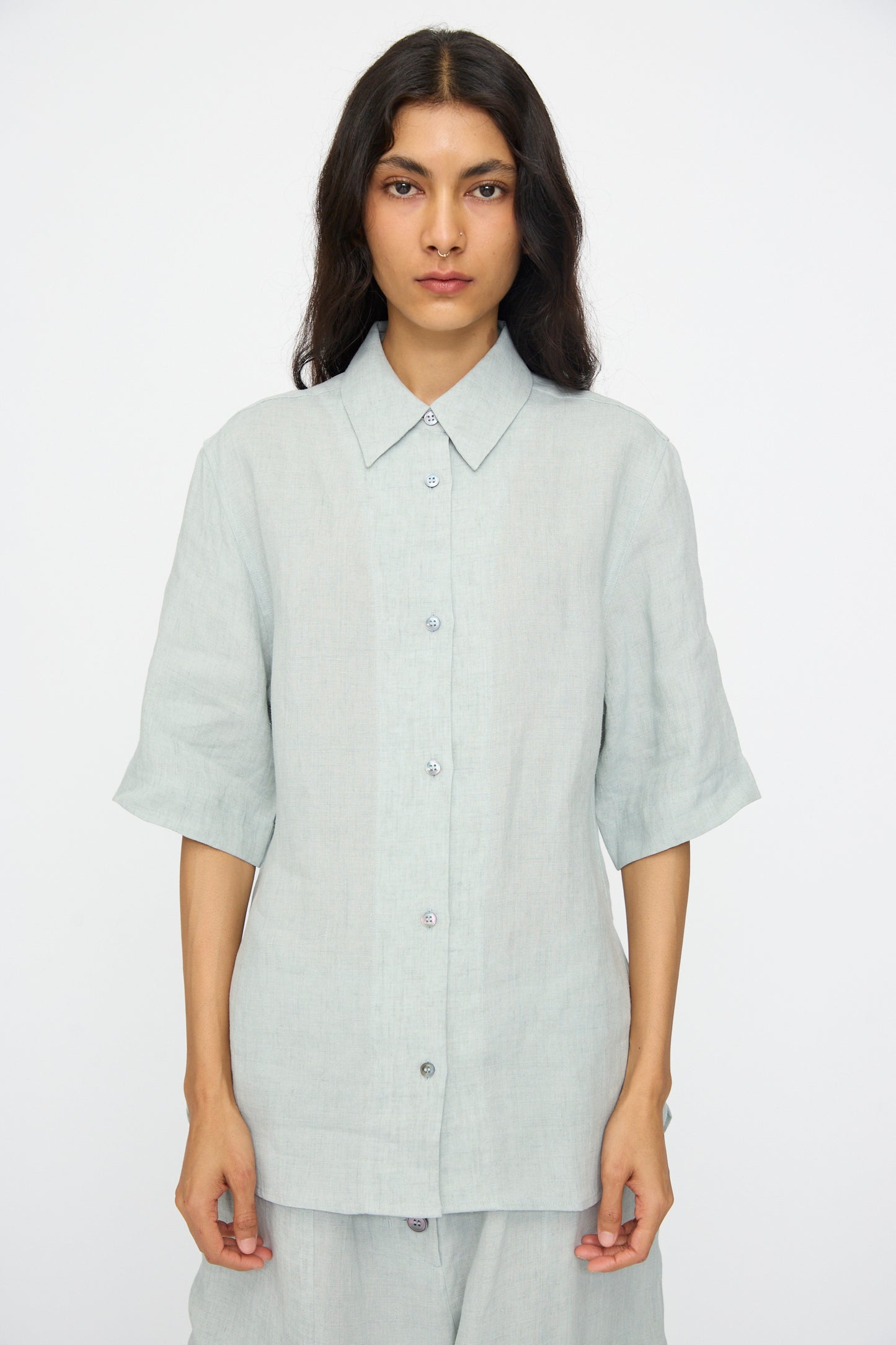 A person wearing the Studio Nicholson Estes Shirt in Spearmint, featuring a relaxed fit and short sleeves, paired with matching pants, stands against a plain white background.