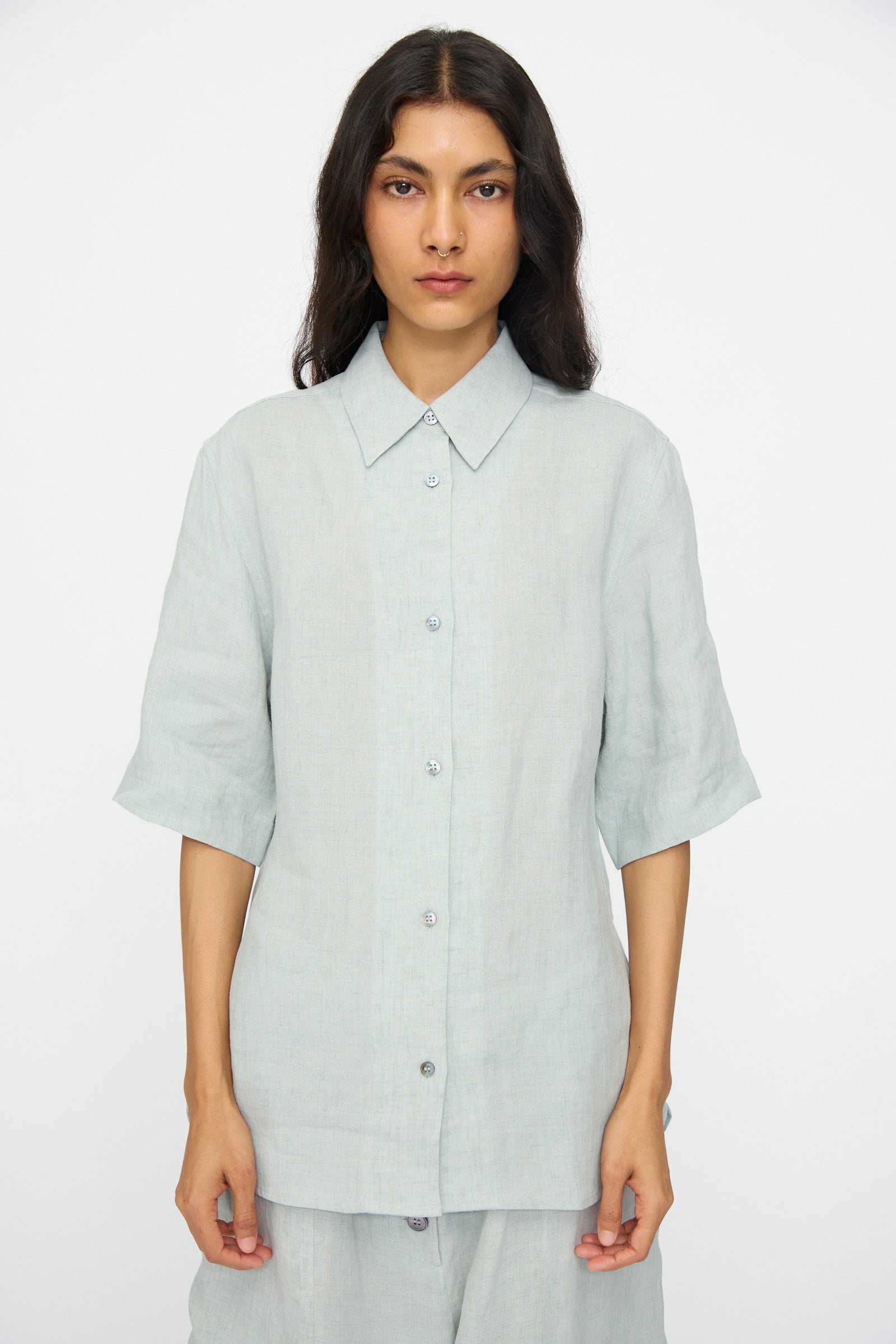 A person wearing the Studio Nicholson Estes Shirt in Spearmint, featuring a relaxed fit and short sleeves, paired with matching pants, stands against a plain white background.