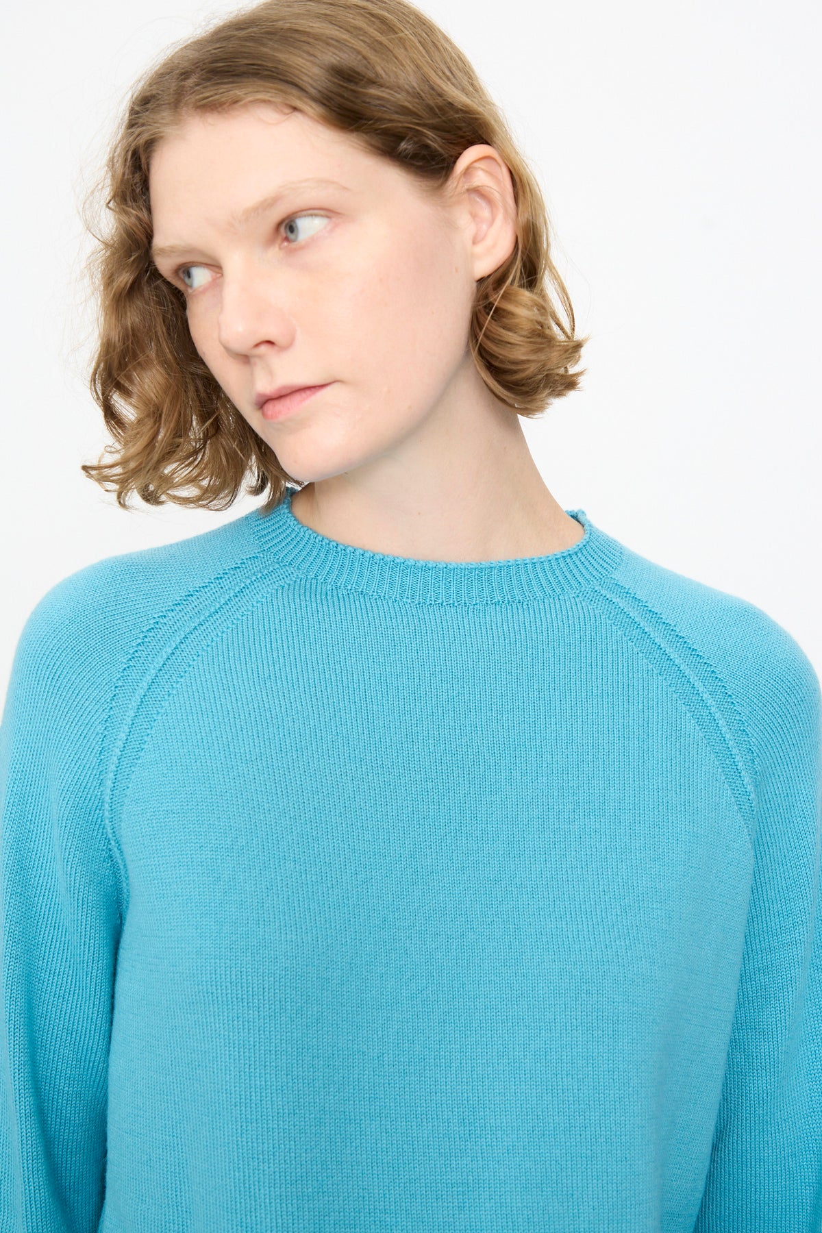 A person with short light brown hair models the Studio Nicholson Extrafine Merino Leonne Sweater in Sky, looking slightly to the left against a plain white background.