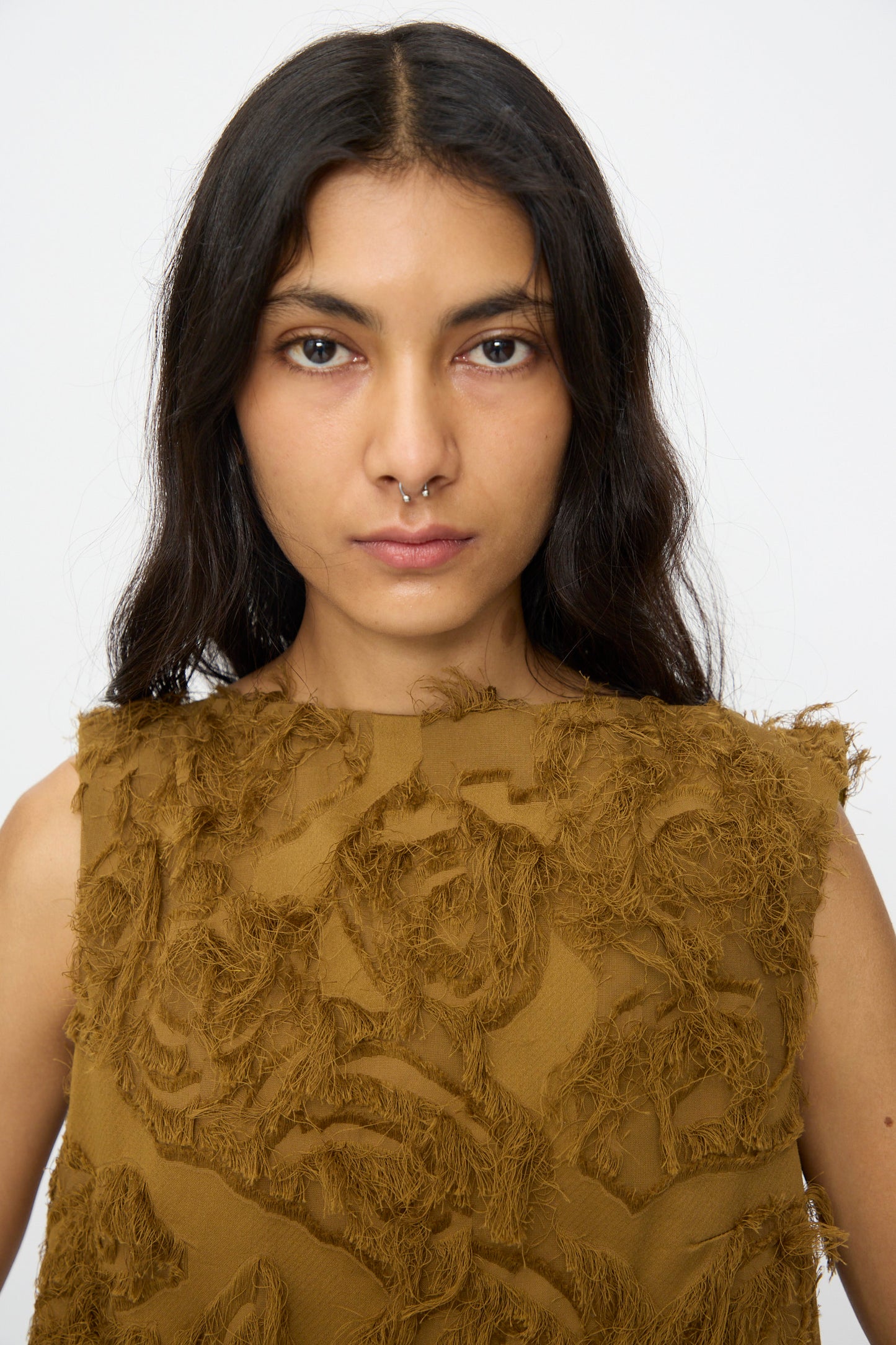 Woman with long dark hair and a septum piercing wears the Studio Nicholson Fringe Jacquard Mager Top in Mustard, standing against a plain white background.