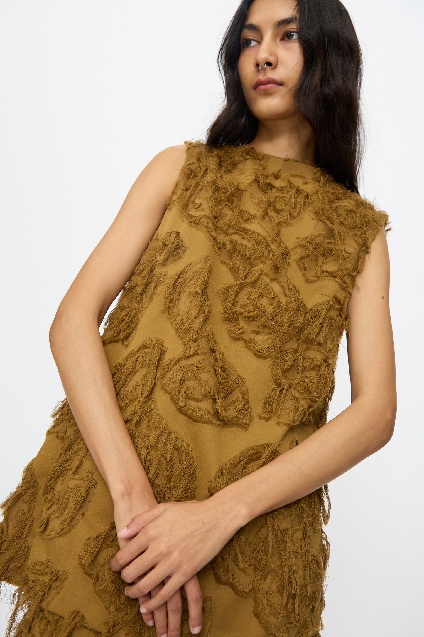A woman models the Studio Nicholson Fringe Jacquard Mager Top in mustard, featuring sleeveless styling and abstract fringed patterns, set against a plain white background.