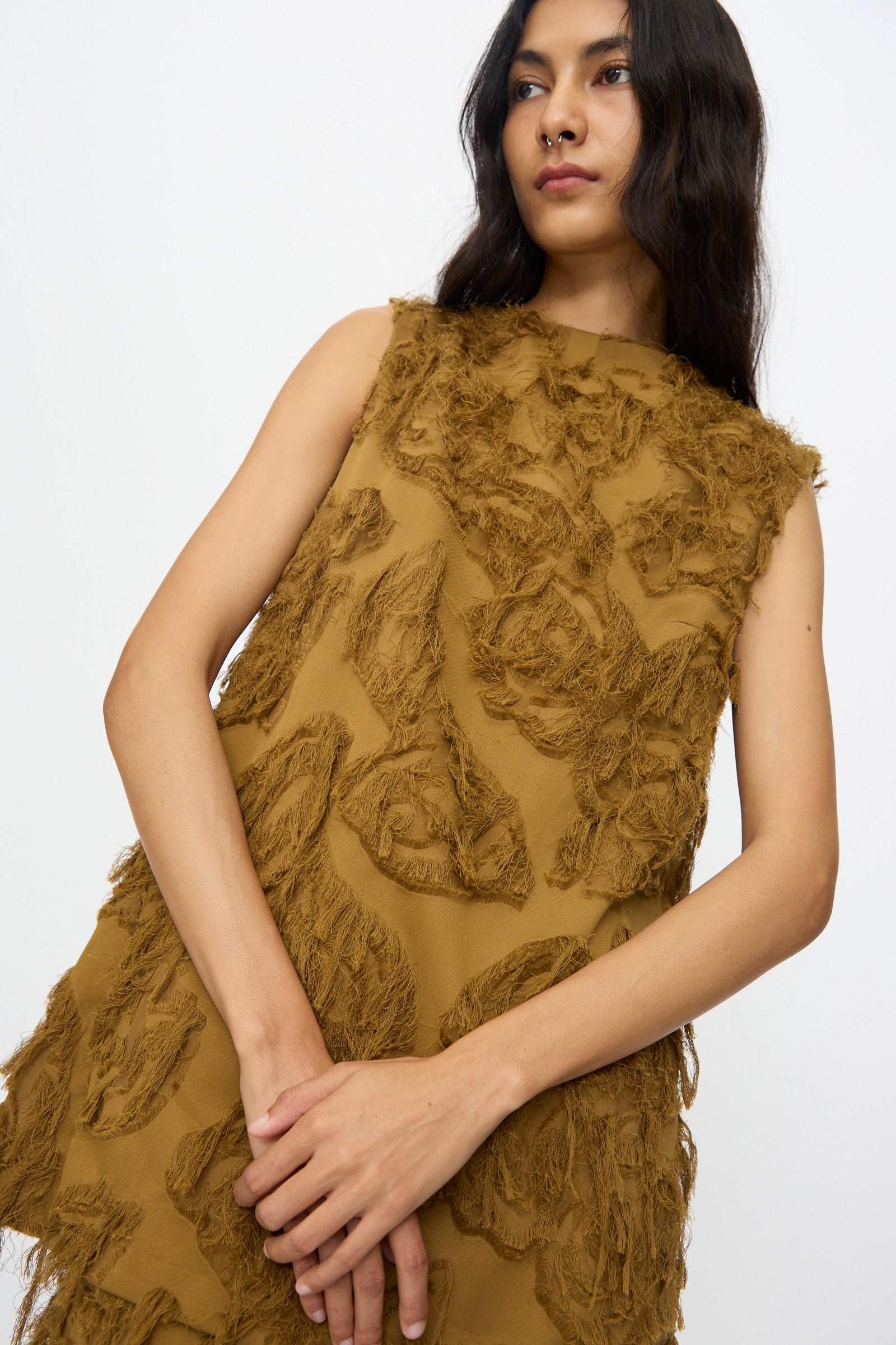 A woman models the Studio Nicholson Fringe Jacquard Mager Top in mustard, featuring sleeveless styling and abstract fringed patterns, set against a plain white background.