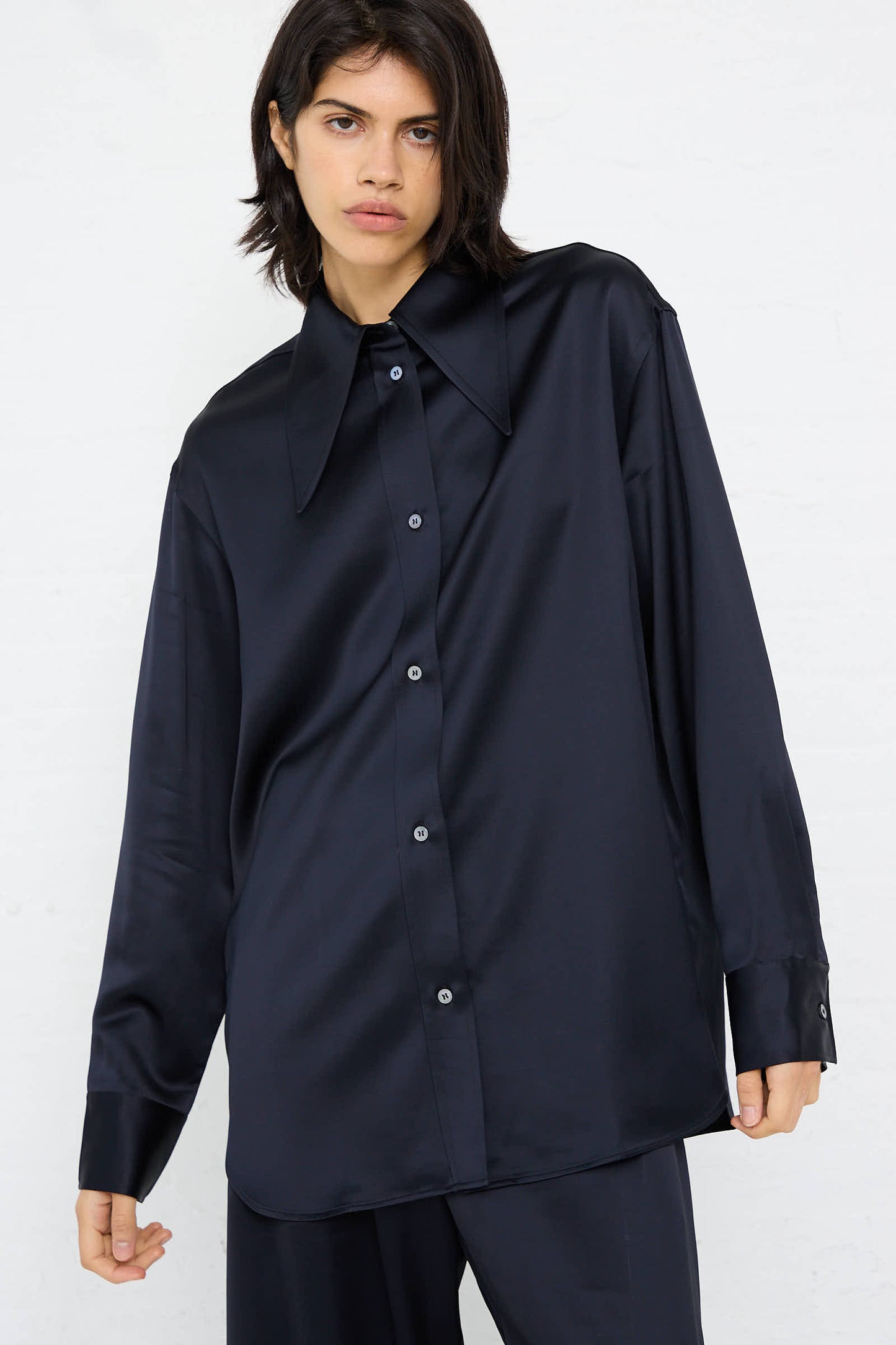 Person wearing Studio Nicholson's Gable Shirt in Black Ink, a relaxed fit, oversized, long-sleeved button-up with large pointed collars, standing against a plain white background.