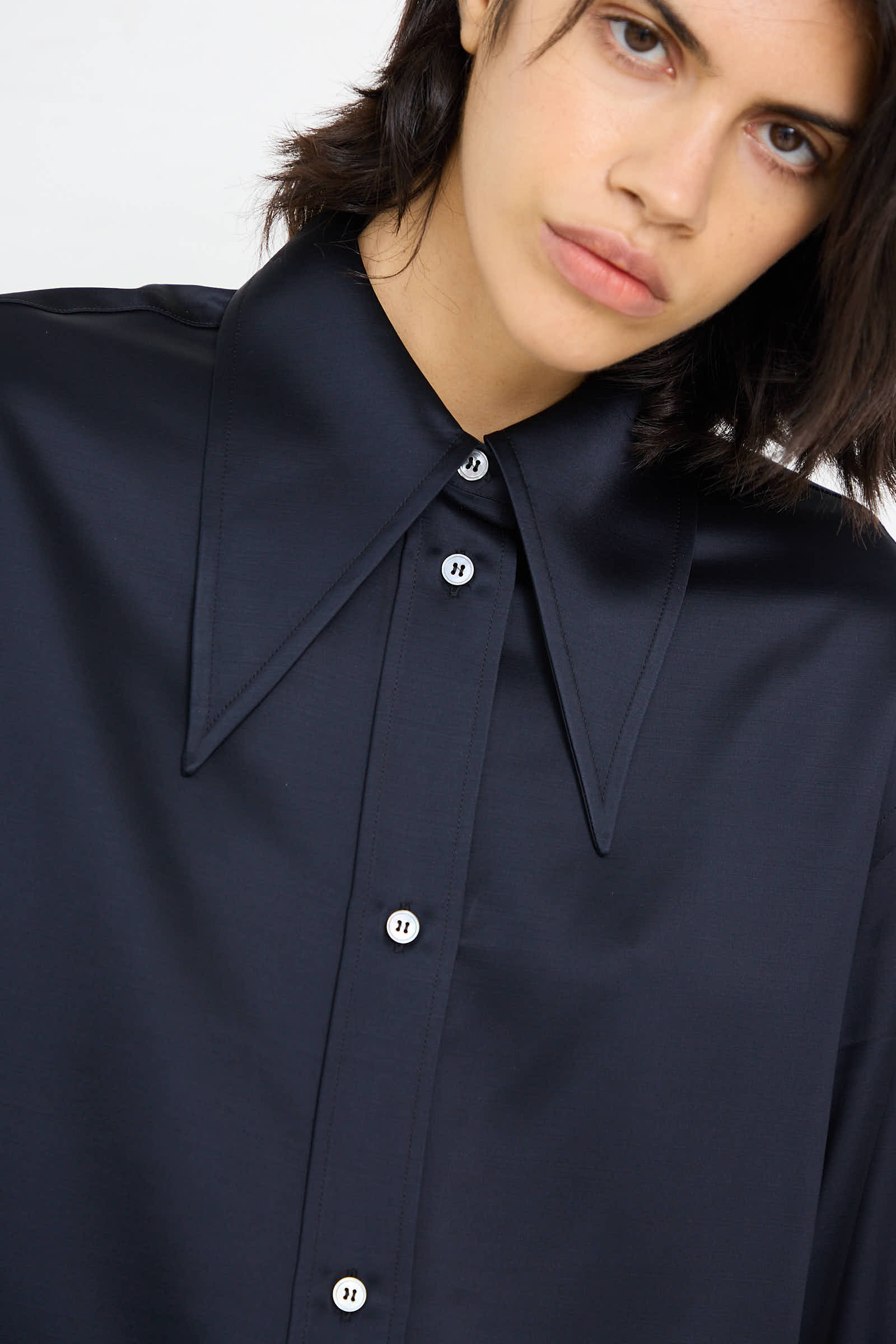 A person wearing the Gable Shirt in Black Ink by Studio Nicholson, featuring a relaxed fit, dark-colored design with a prominent wide collar and buttoned front.