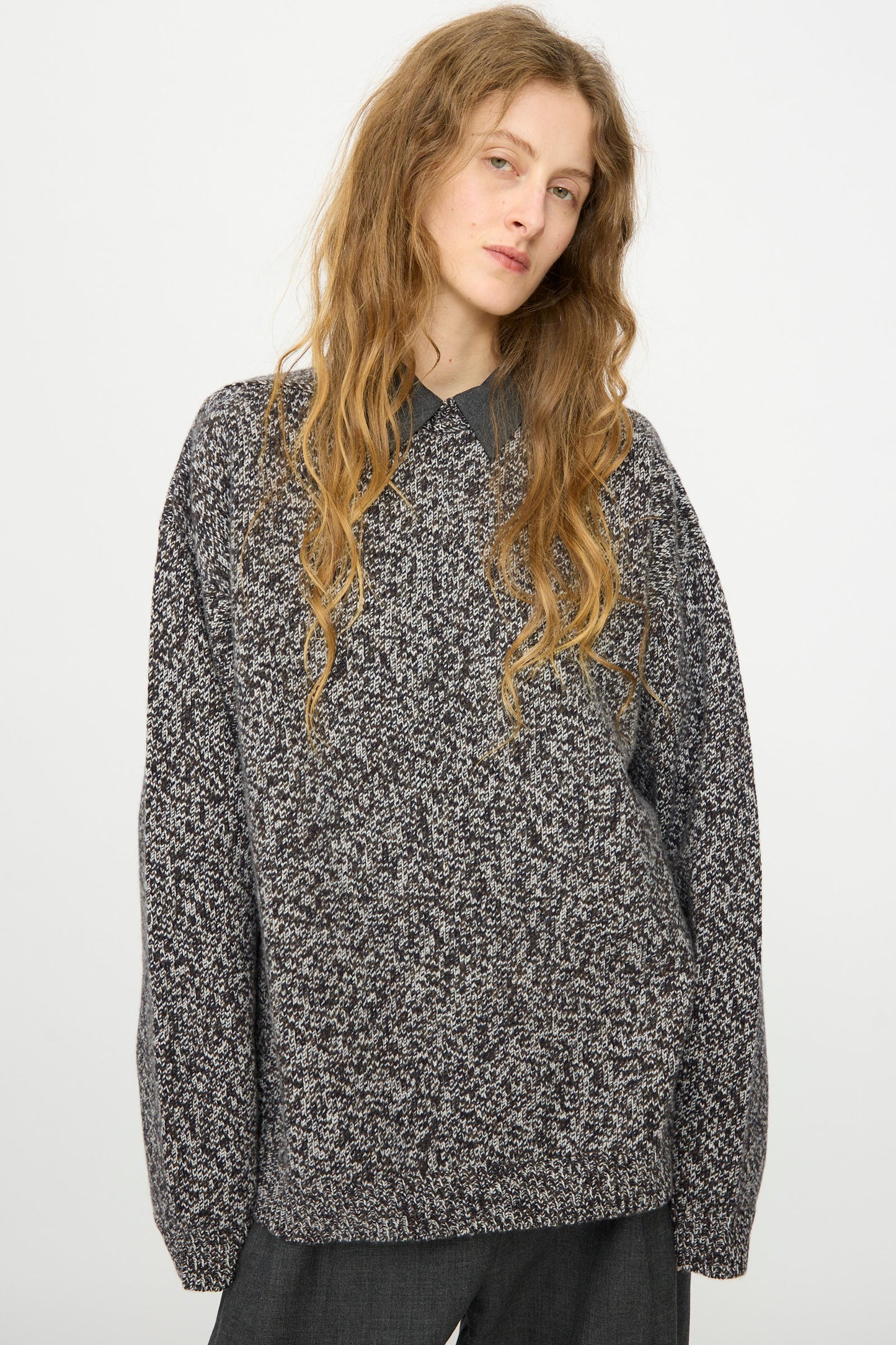 A person with long wavy hair wears the Studio Nicholson Hemyl Guernsey Jumper in Navy Mouline over a collared shirt, standing against a plain white background.