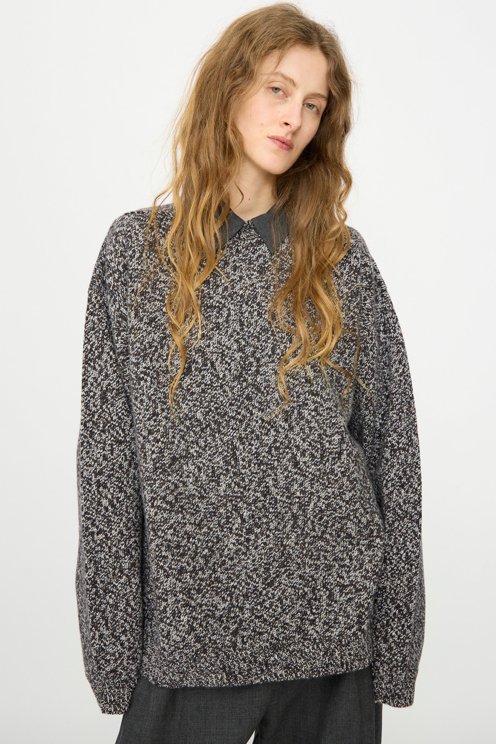 A person with long wavy hair wears the Studio Nicholson Hemyl Guernsey Jumper in Navy Mouline over a collared shirt, standing against a plain white background.