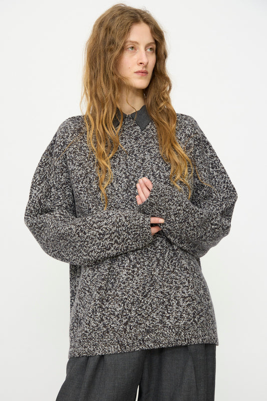 Person with long wavy hair wears the Studio Nicholson Hemyl Guernsey Jumper in Navy Mouline, made in London, layered over a collared shirt and dark trousers, standing against a plain white background.