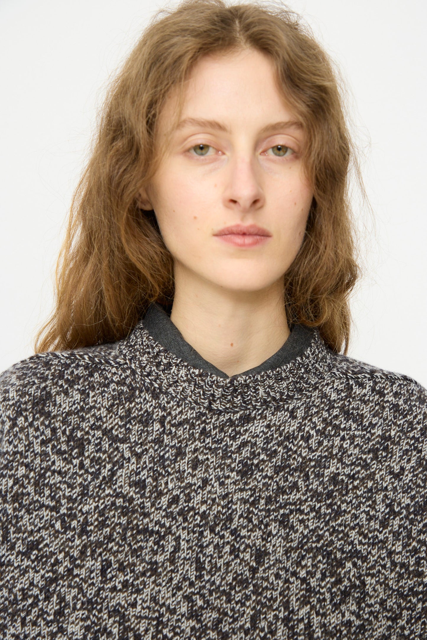 A person with long, wavy light brown hair wears the Studio Nicholson Hemyl Guernsey Jumper in Navy Mouline and looks directly at the camera against a plain background.