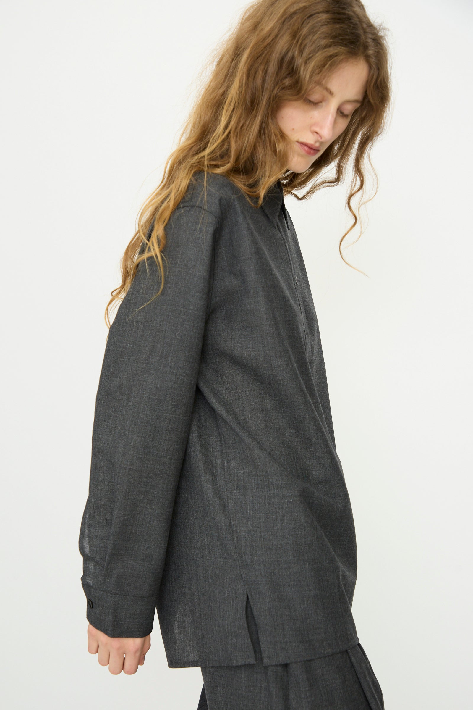 Model with long, wavy hair wears the Studio Nicholson Heritage Wool Pinole Shirt in Slate Melange, shown against a plain white background.