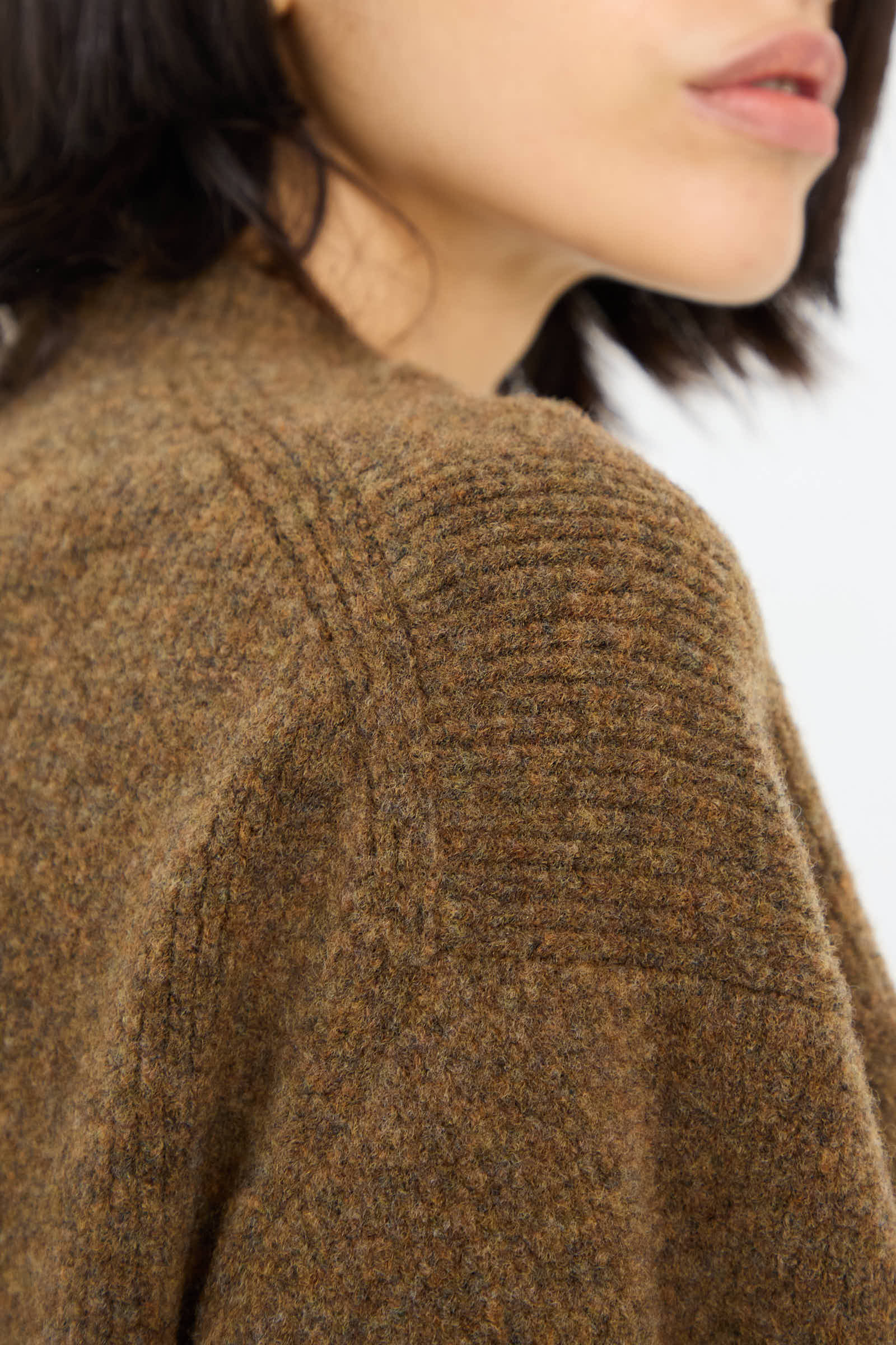 Close-up of a person wearing the Studio Nicholson High Loft Wool Sirio Crew Neck in Nutmeg, highlighting the detailed stitching on the shoulder seam. The person's face is partially visible, drawing attention to the relaxed fit of the textured brown knit merino wool blend sweater.