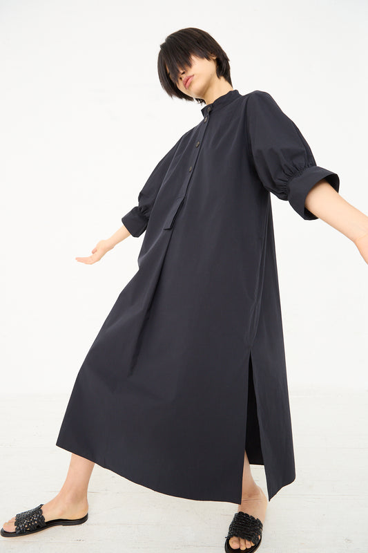 A person in a Knoll Shirt Dress with Ruched Cuff in Darkest Navy by Studio Nicholson striking a playful pose against a white background.