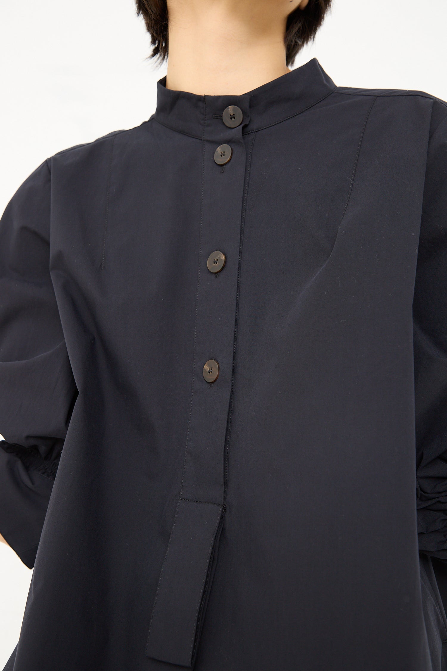 Close-up of a person wearing a Studio Nicholson Knoll Shirt Dress with Ruched Cuff in Darkest Navy with visible button details and a standing collar.