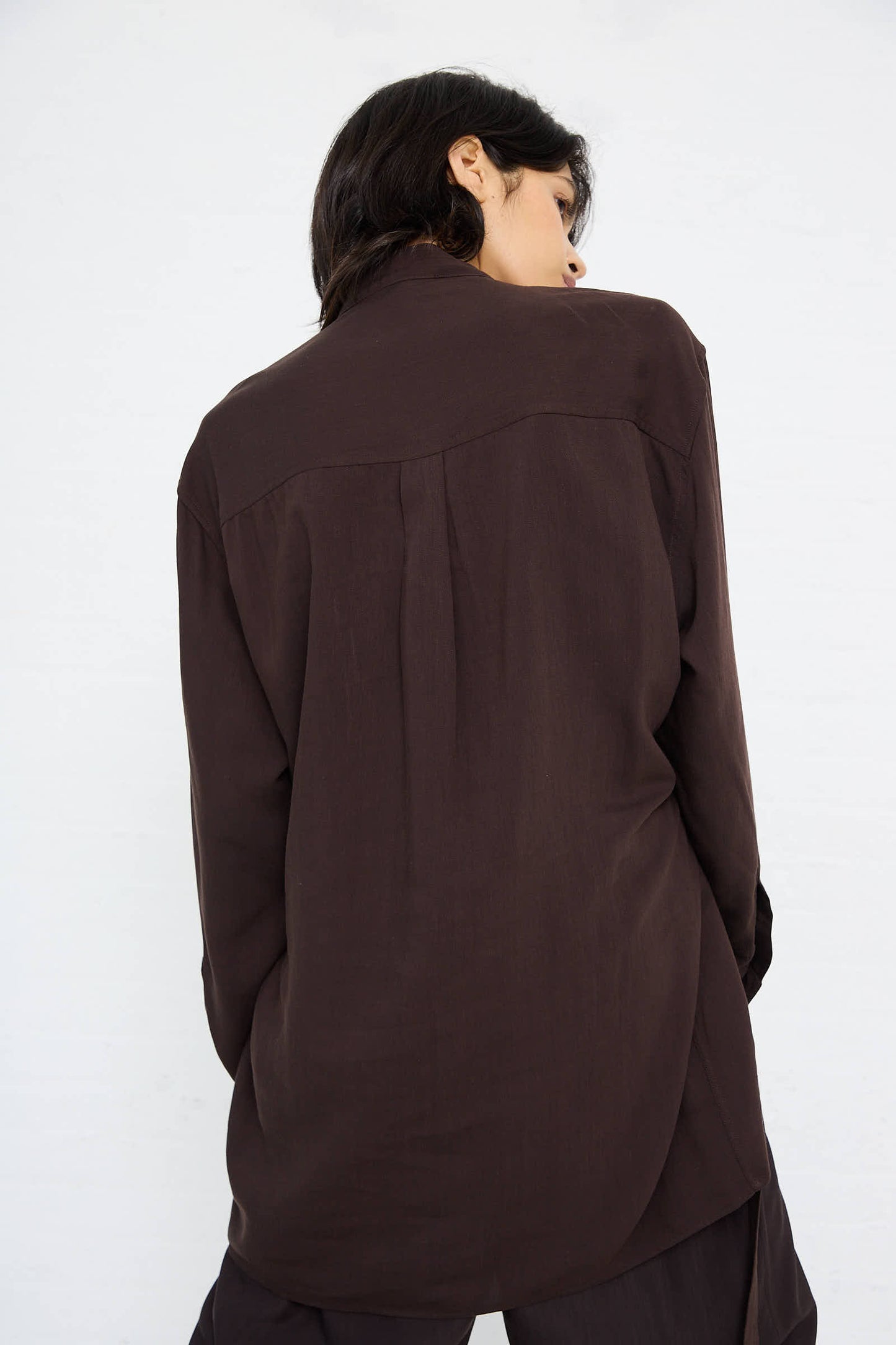 Person facing away from the camera, wearing a Lane Collarless Shirt in Espresso by Studio Nicholson against a plain background.