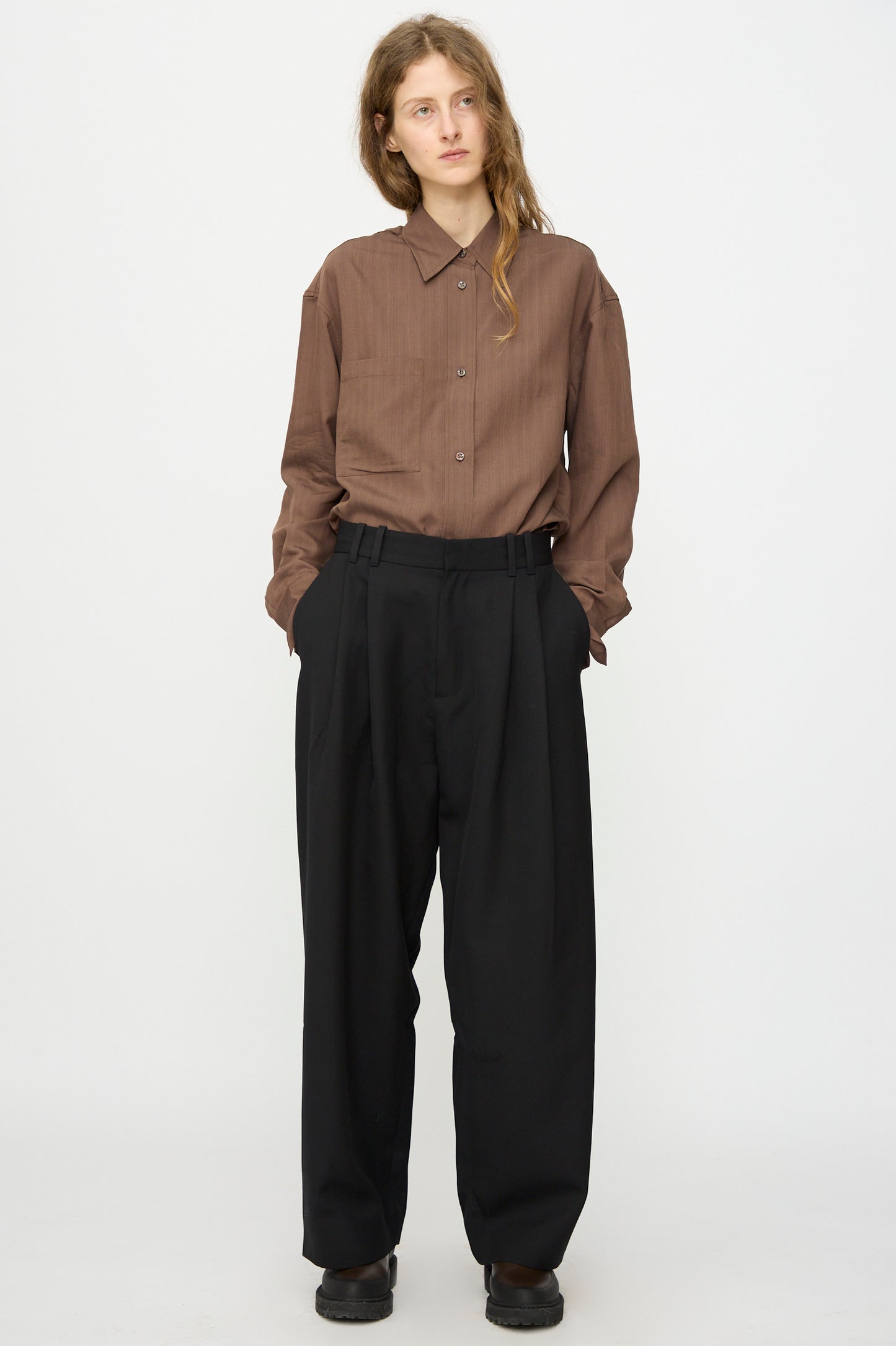 Person stands against a white background, hands in pockets, wearing Studio Nicholson's Light Tech Wool Line Pant in Black—high-waisted with a slouchy yet tailored finish.