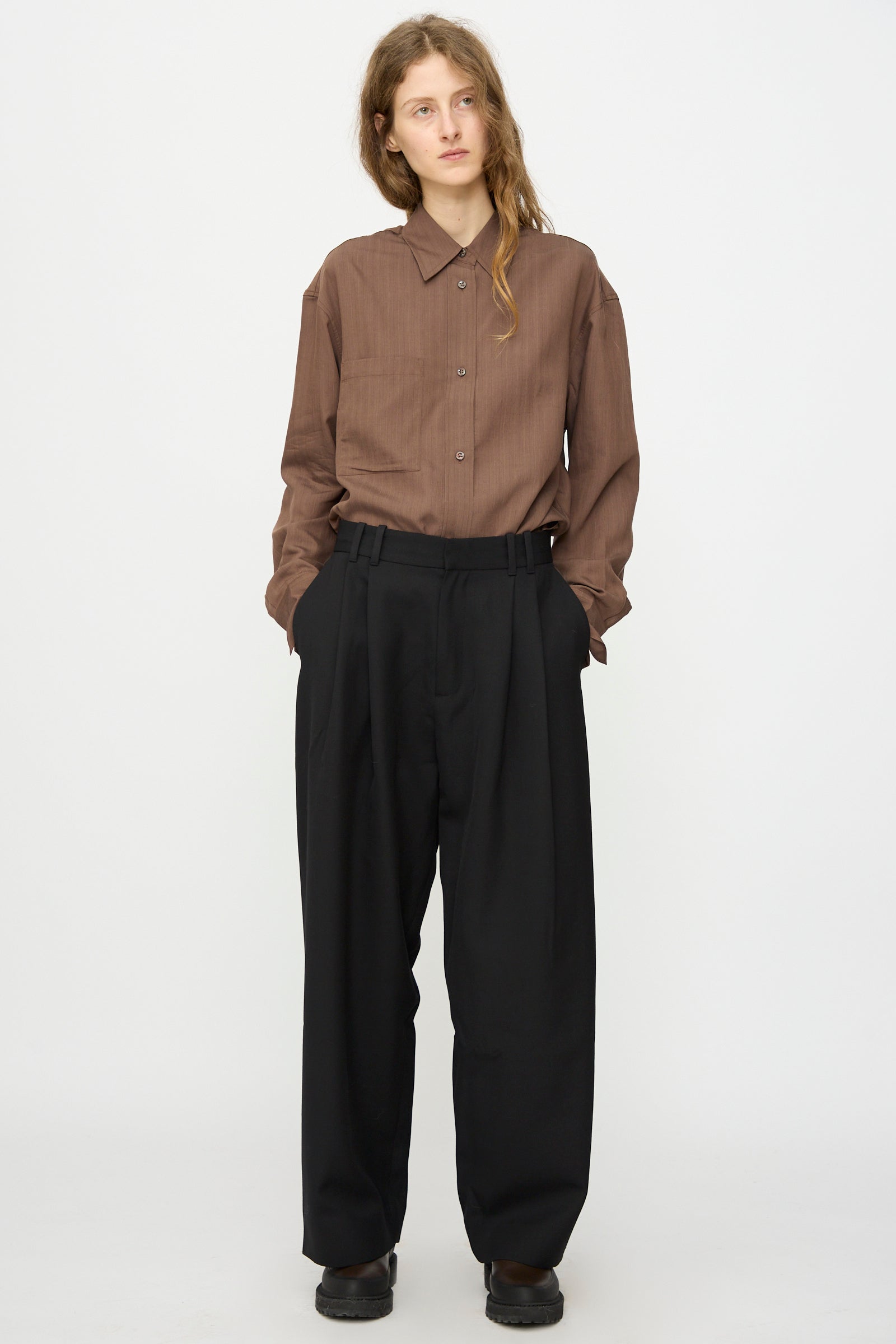 Person stands against a white background, hands in pockets, wearing Studio Nicholson's Light Tech Wool Line Pant in Black—high-waisted with a slouchy yet tailored finish.