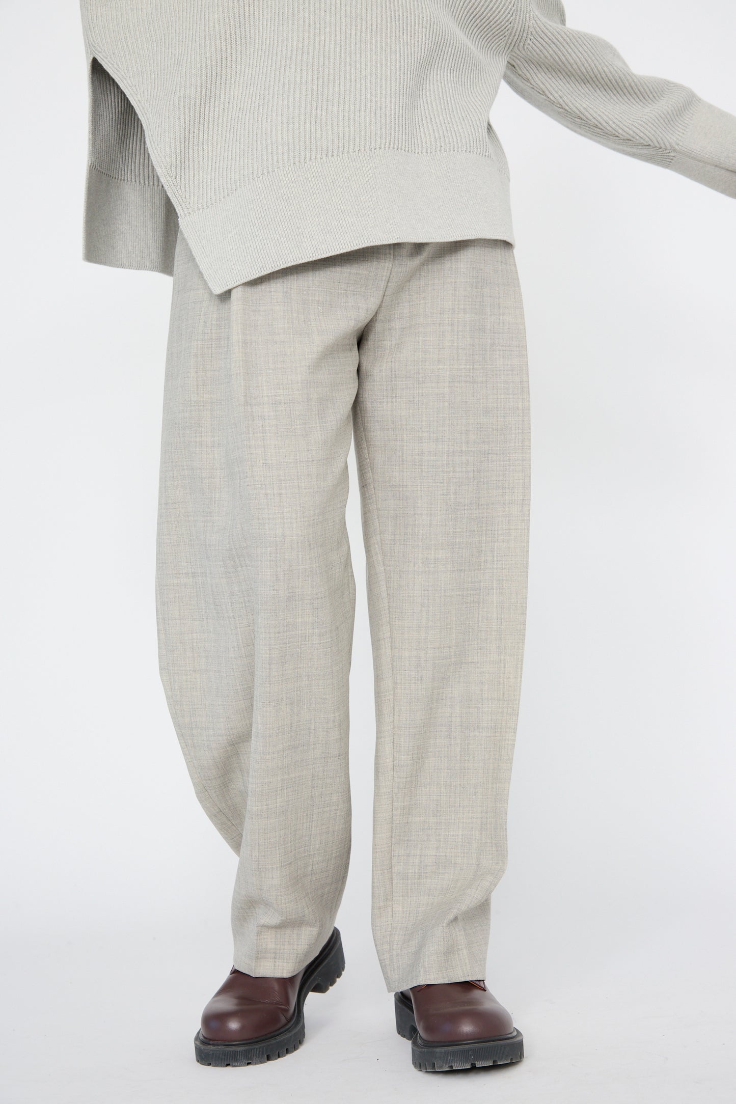 A person wearing Studio Nicholson's Lightweight Tropical Wool Vai Trouser in Ice Melange, paired with a matching oversized sweater and brown shoes, is standing against a white background.