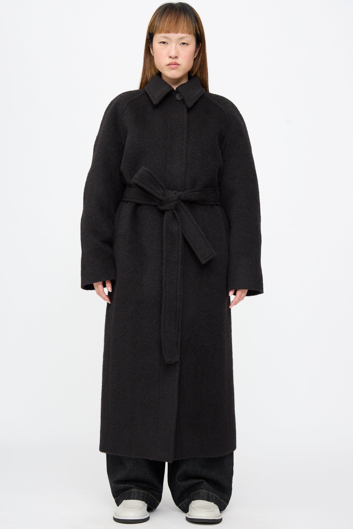 A person wearing a cola-colored Studio Nicholson Mohair Kober Coat, an oversized long wool design with a belt and collar.